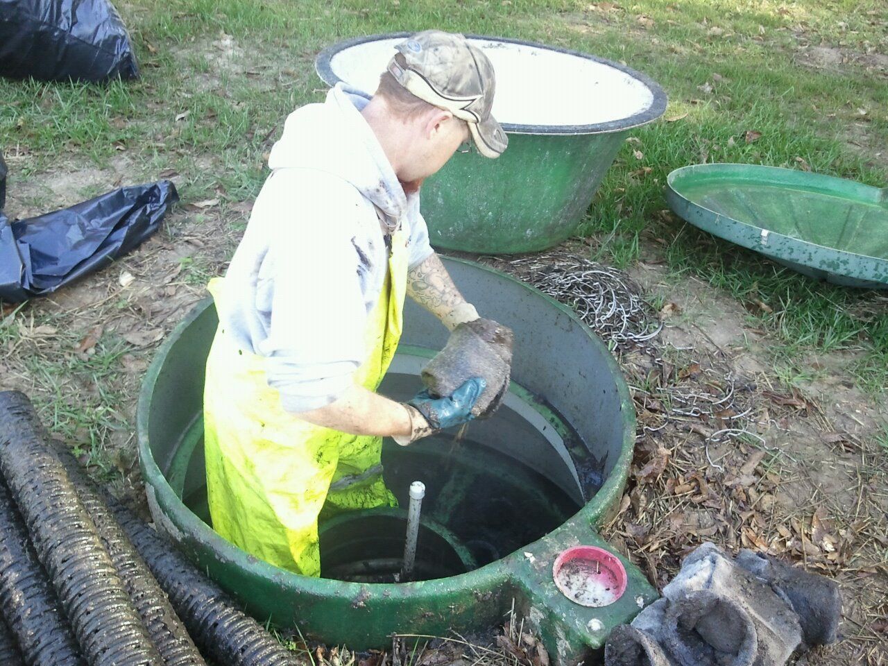 Man in yellow protective gear working inside a septic tank, surrounded by equipment.
