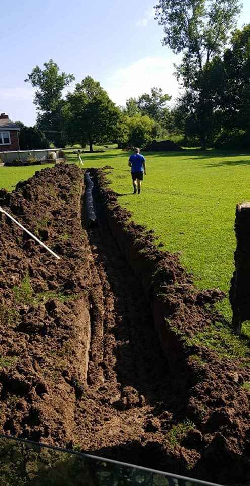 A deep trench dug in a grassy yard. A person in blue stands in the distance.