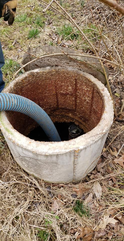 A septic tank being serviced: a hose extends into an open concrete cylinder.