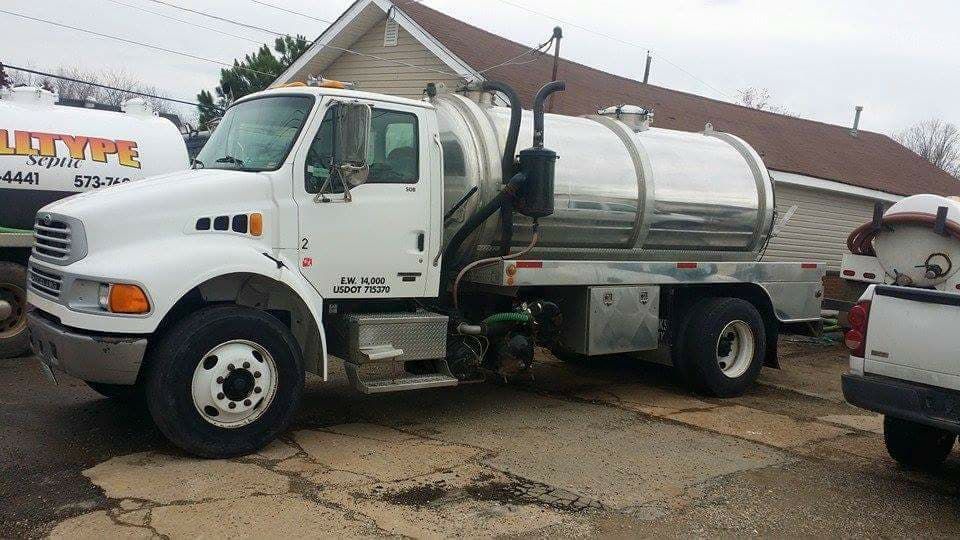 White sanitation truck with silver tank parked outside a building.