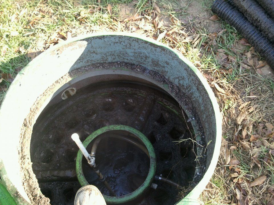 Open green septic tank, with visible water, green hose, and black corrugated pipe nearby.