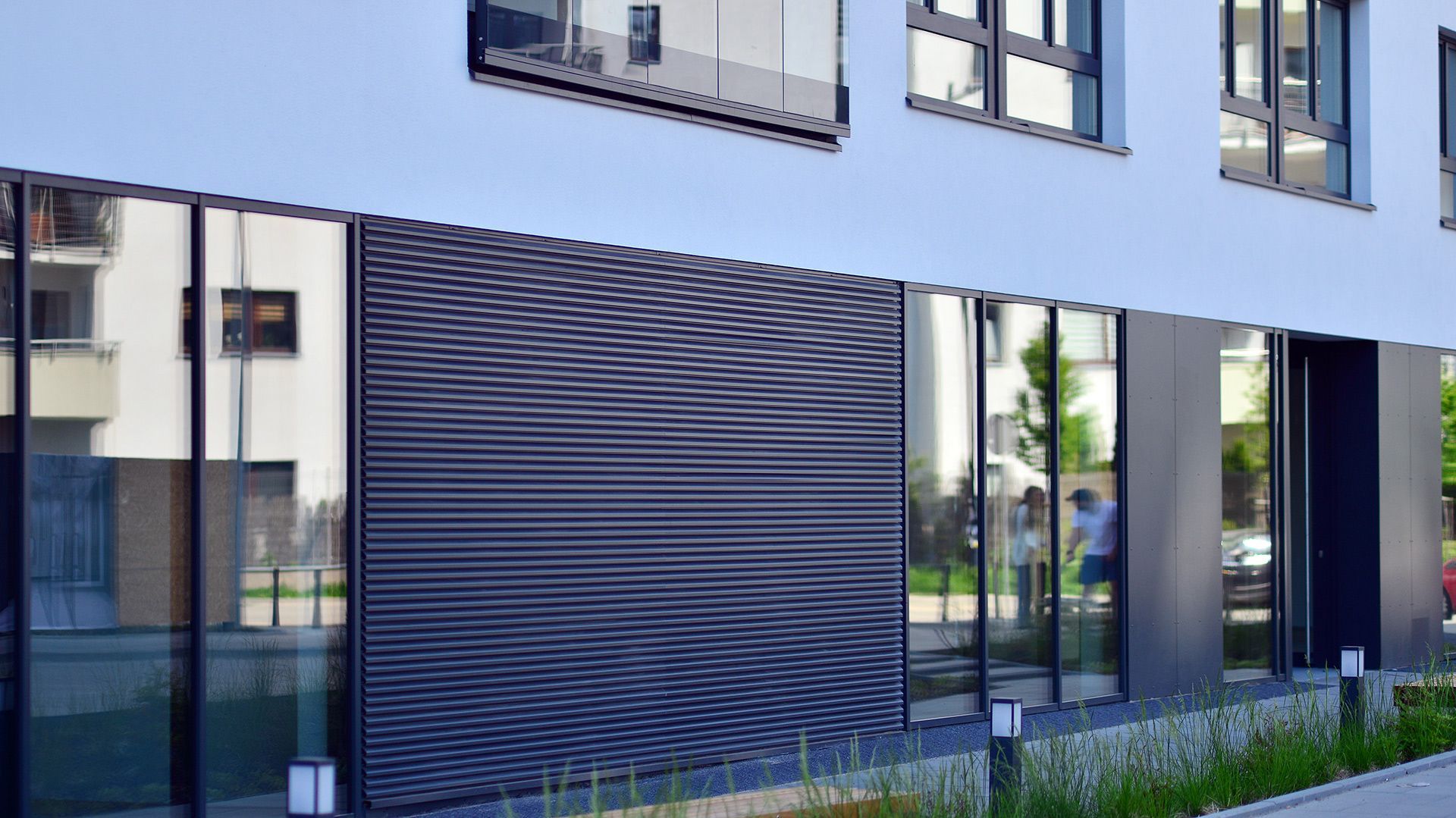 Modern building exterior with large glass windows reflecting the surroundings, and a dark, textured panel.