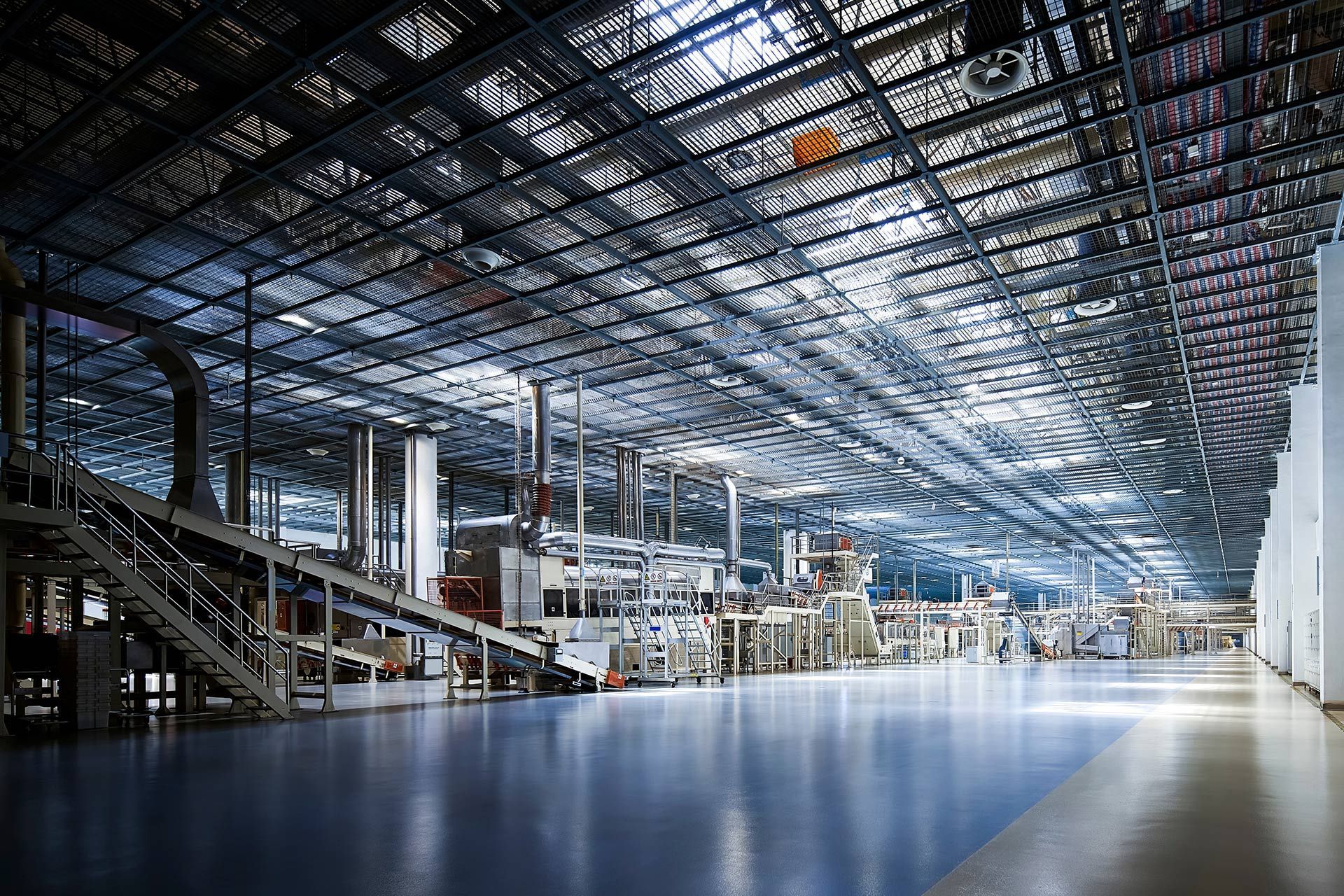 Large industrial factory interior with machinery, a polished floor, and a metal grid ceiling.