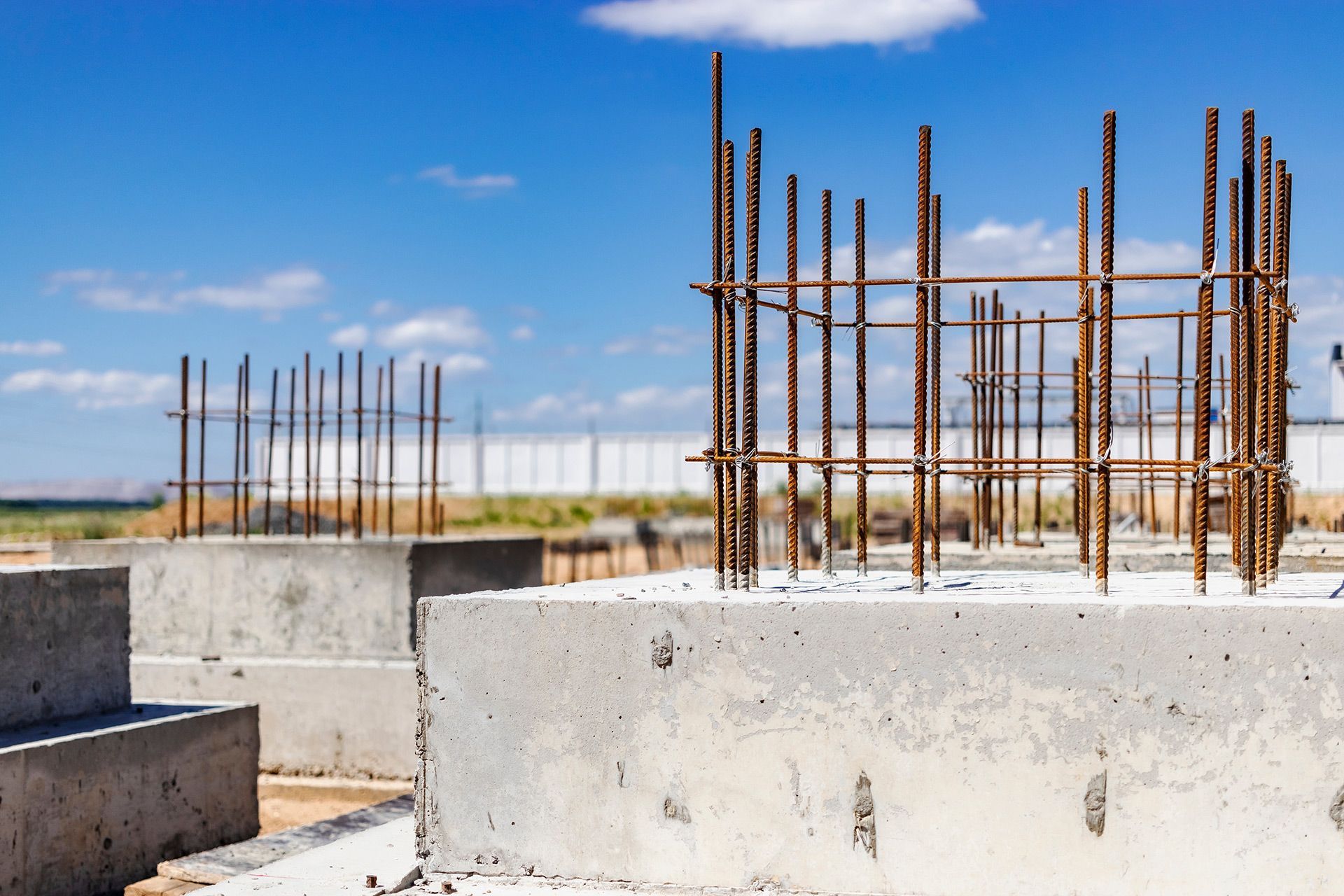 Concrete foundations with rebar structures, on a construction site under a blue sky.