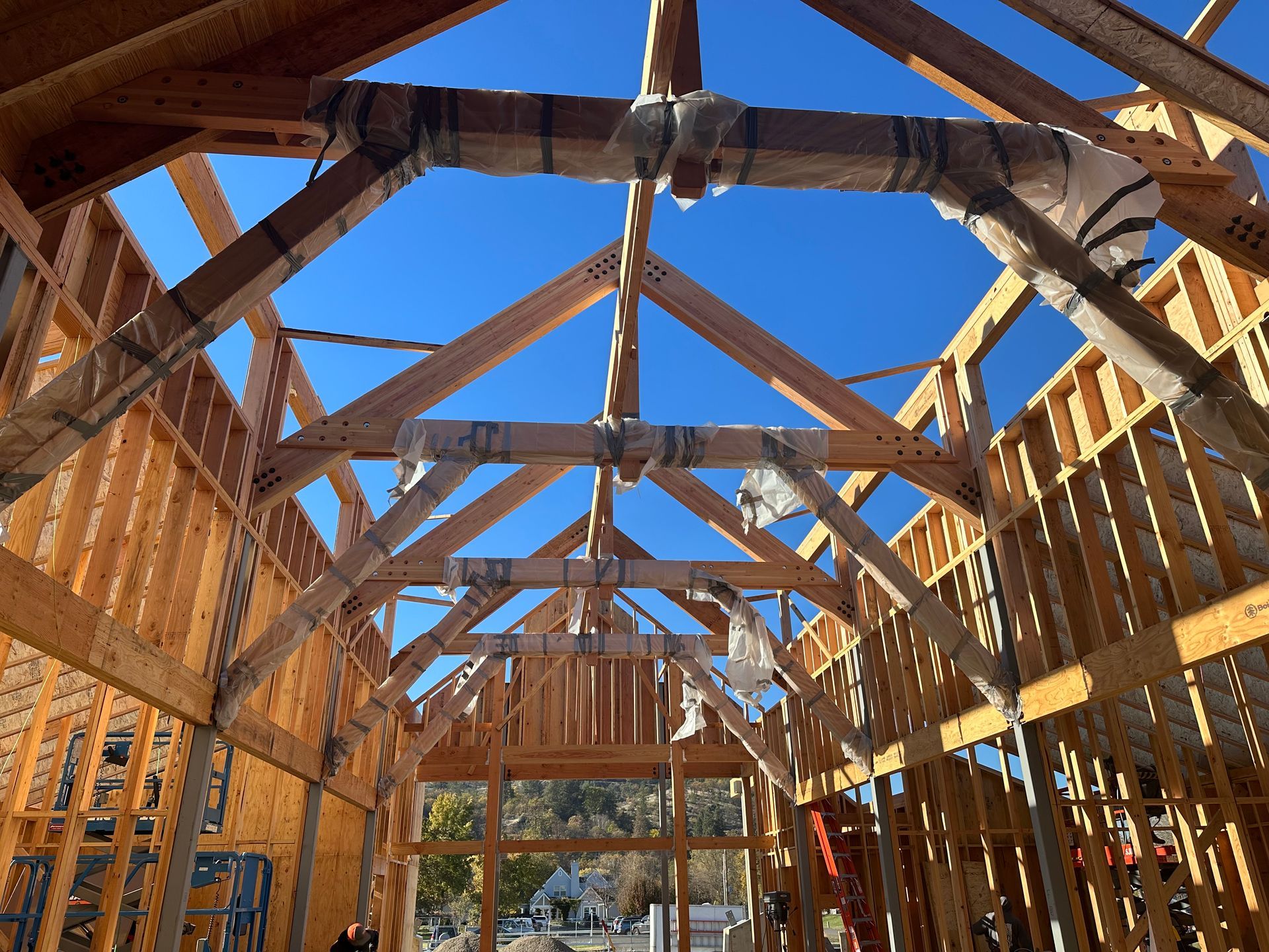 Two construction workers on an orange lift are assembling a metal roof frame, under a cloudy sky.
