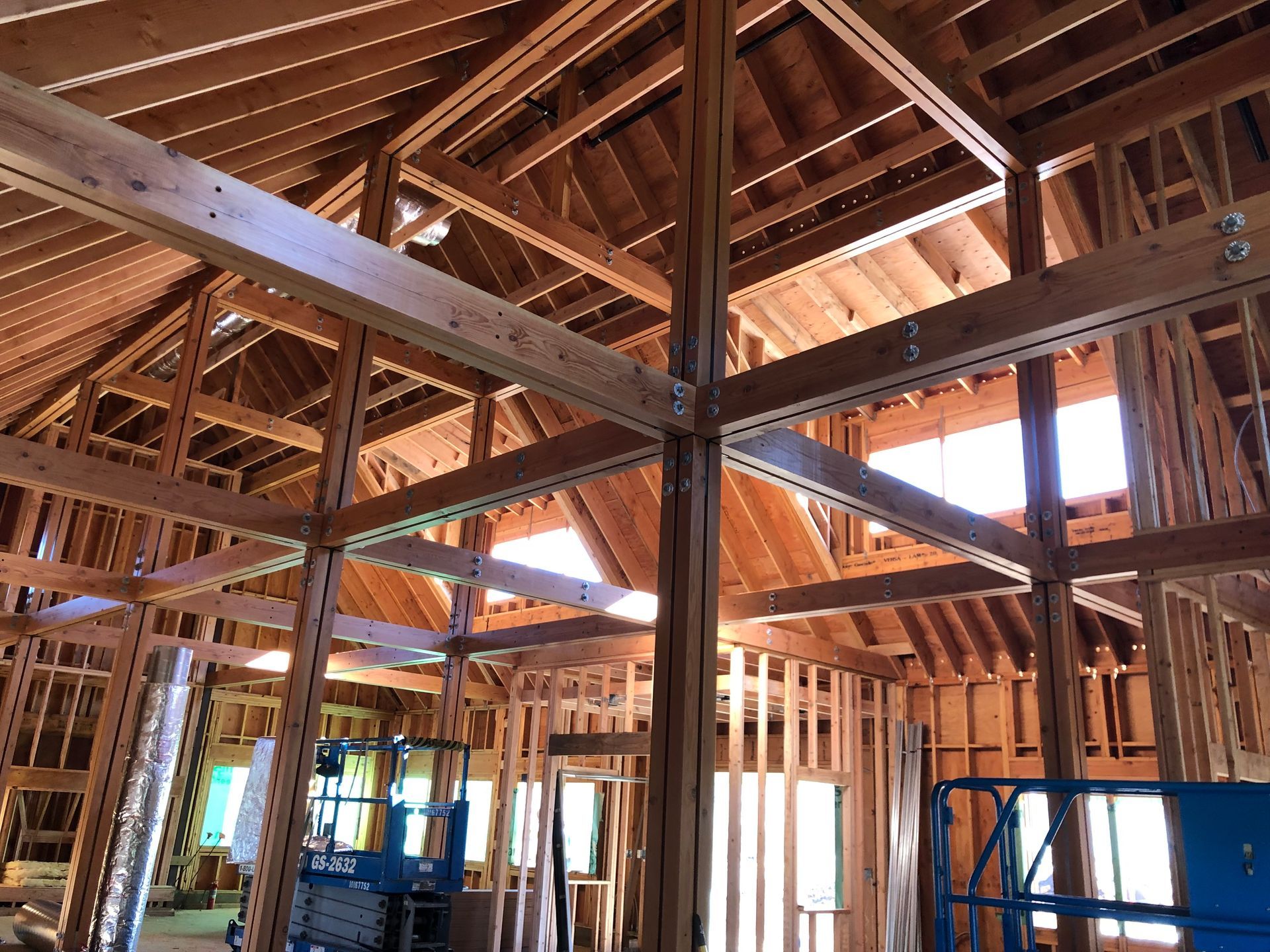 Interior wood framing of a building under construction, showing rafters, beams, and windows.