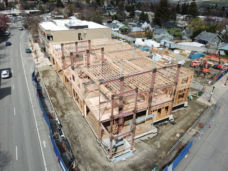 Construction site, two-story building frame with steel beams and wooden beams, next to a street with cars.