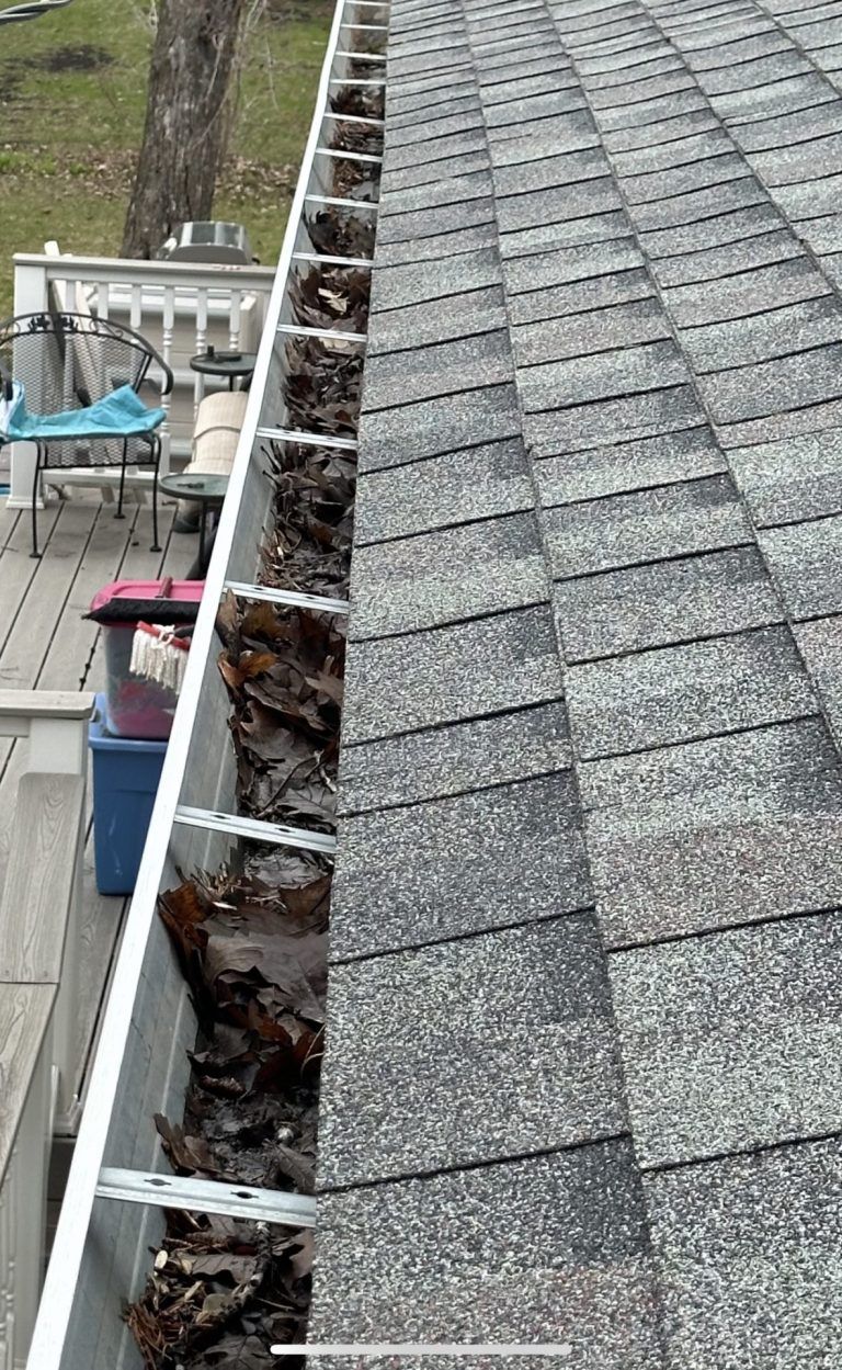 A gutter with leaves on it is on the roof of a house.