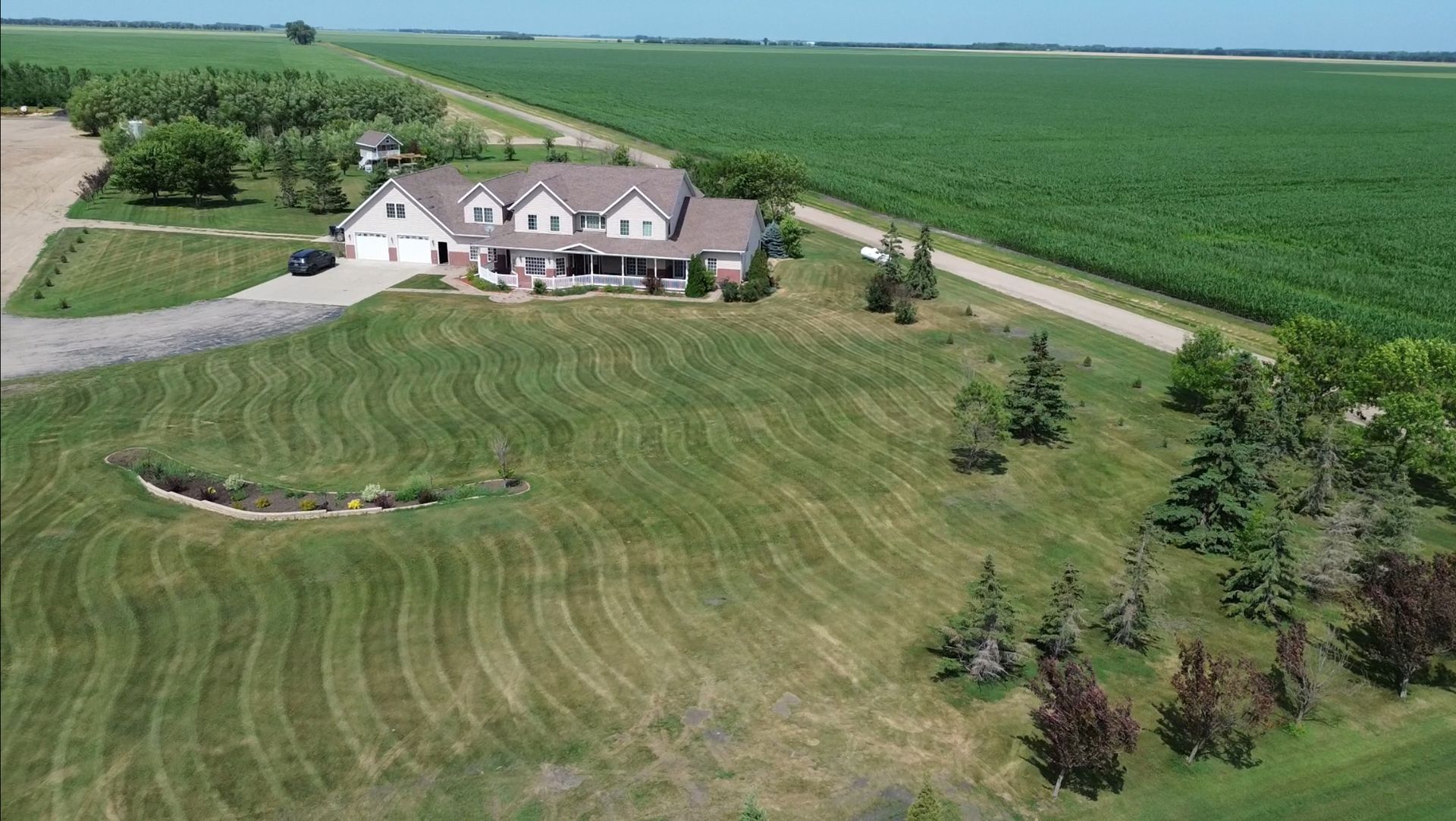 Large house with well-manicured lawn, bordered by farmland, under a bright blue sky.