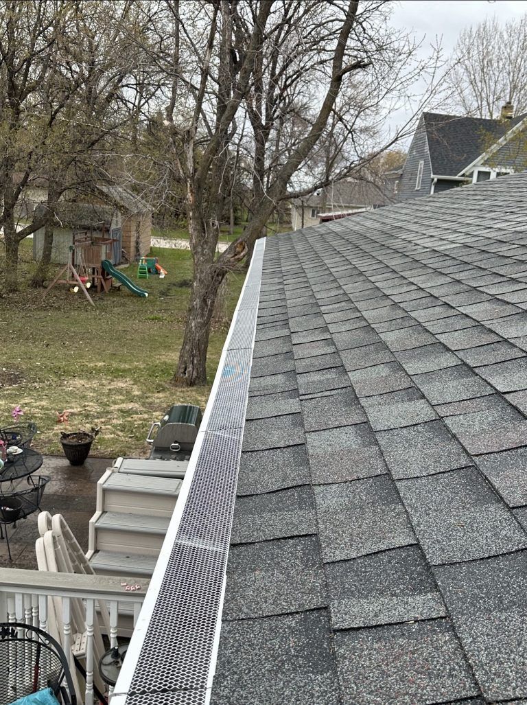 A close up of a gutter on a roof with trees in the background.