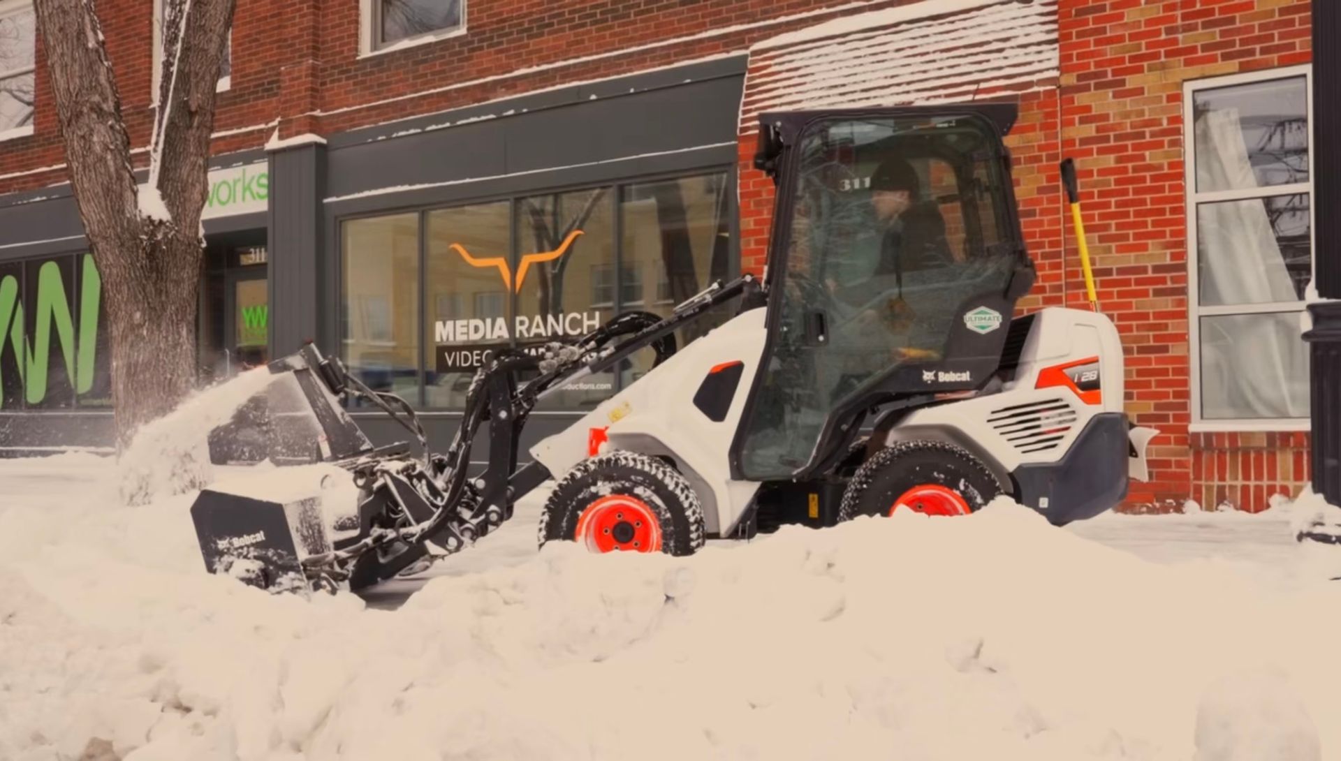 A person walks down a snow-covered path next to a wooden fence and trees on a winter day.
