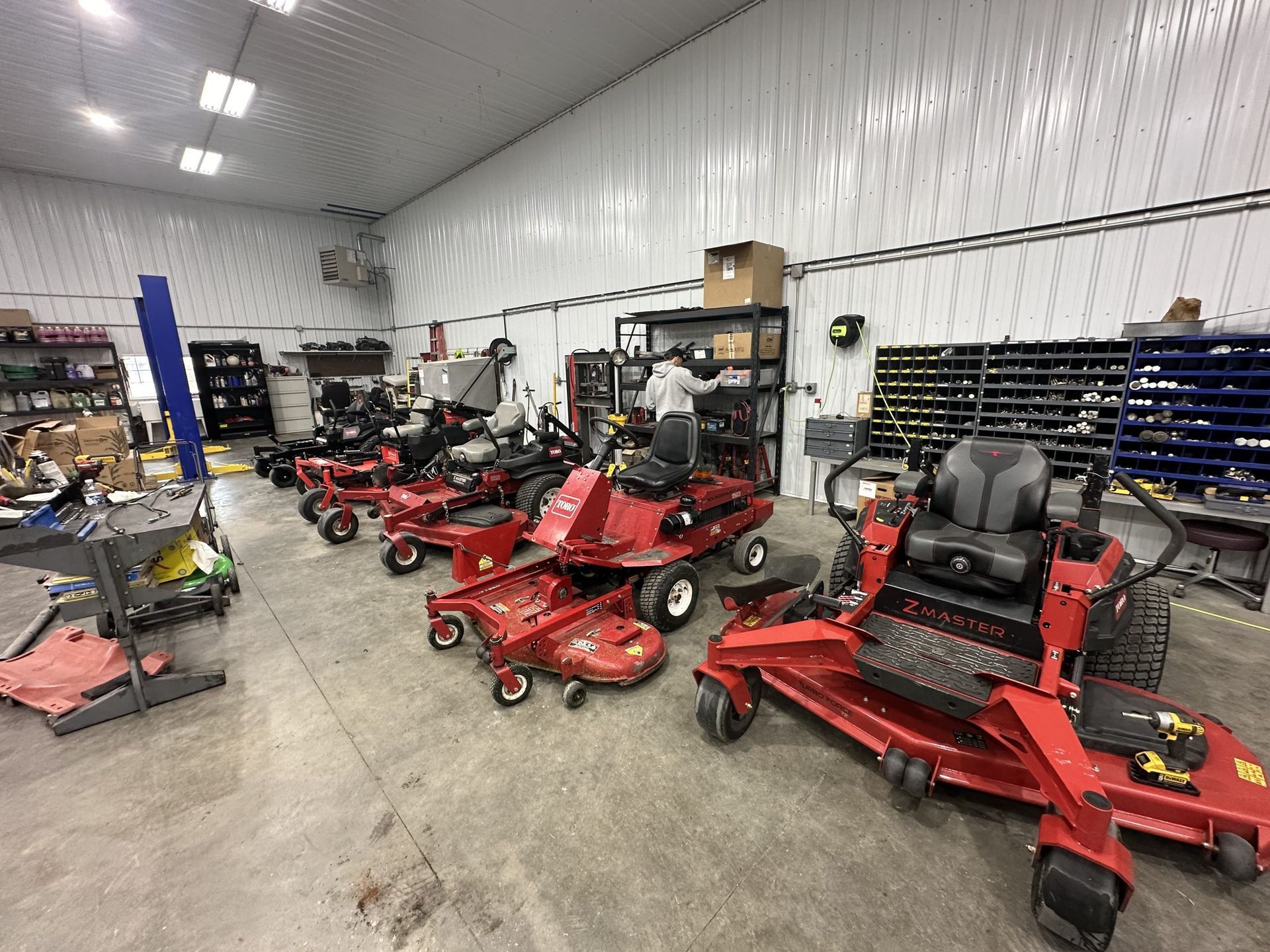 A row of lawn mowers are lined up in a garage.