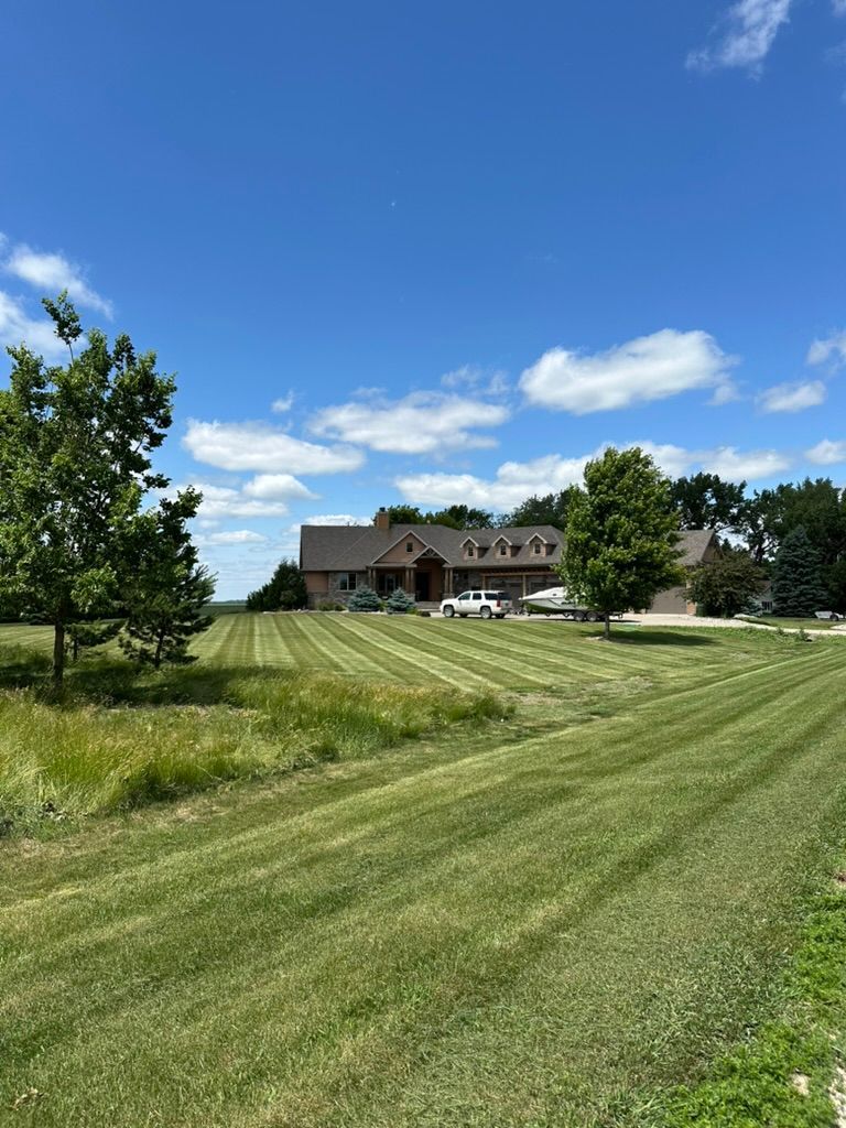 Large house with manicured lawn under a blue sky with fluffy clouds; a sunny day.