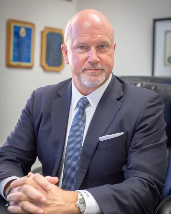 A man in a suit and tie is sitting in a chair with his hands folded.