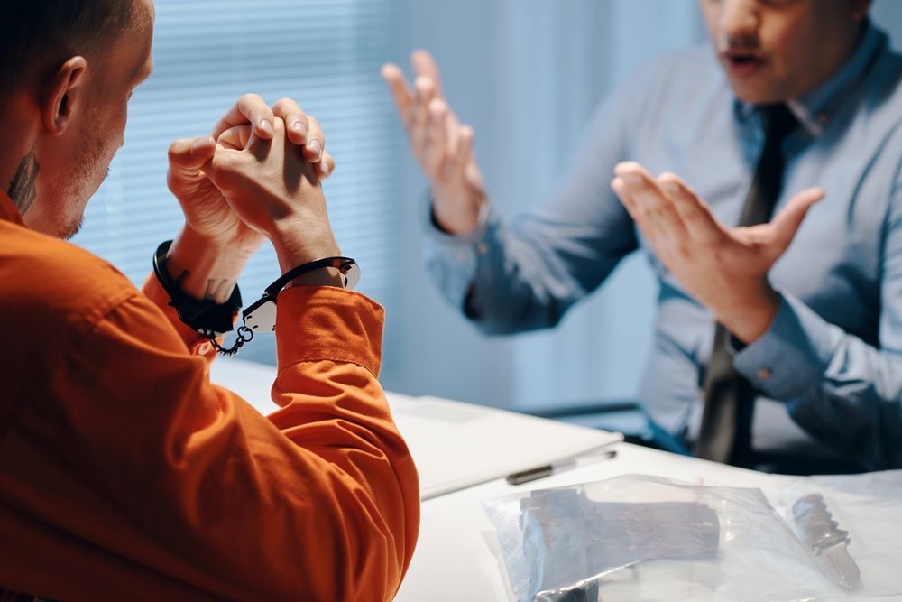 A man in handcuffs is sitting at a table talking to a man in a suit.