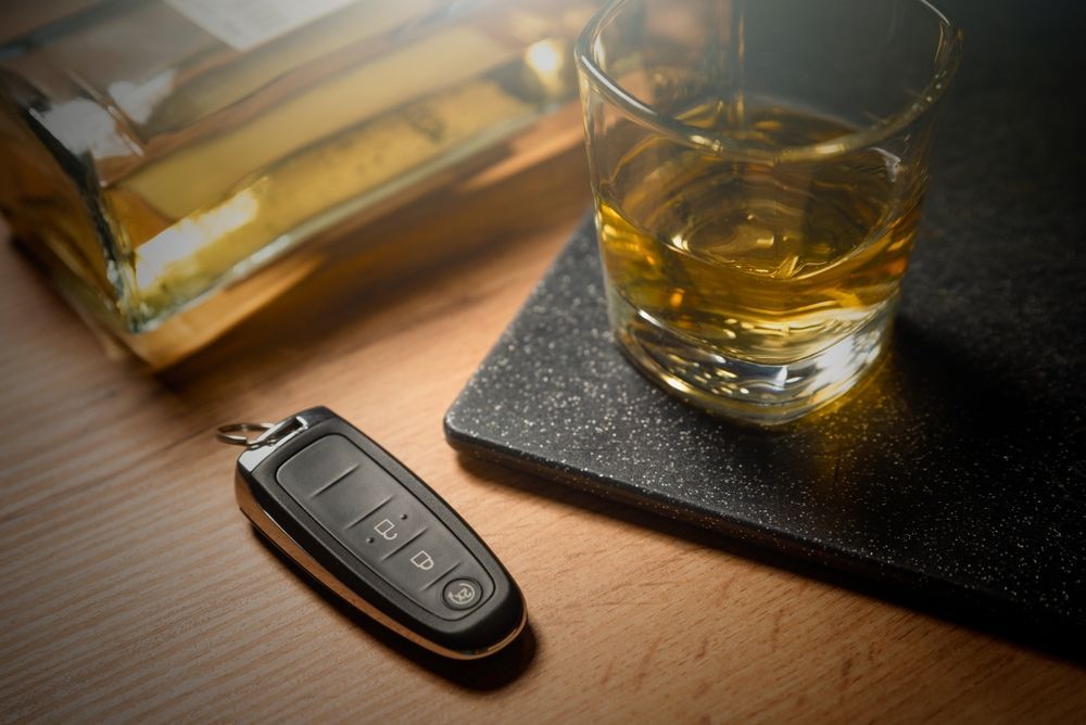 A car key next to a glass of whiskey and a bottle of whiskey.