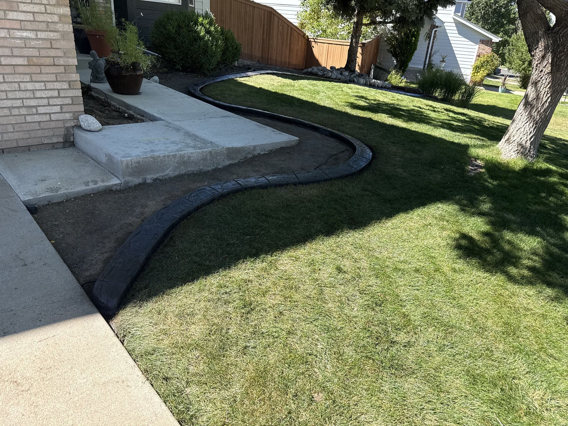 Person installing a curved concrete border around a tree in a yard.