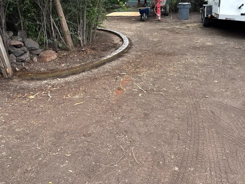 Dirt driveway with a curved edge, a person with a wheelbarrow, and a trash can.