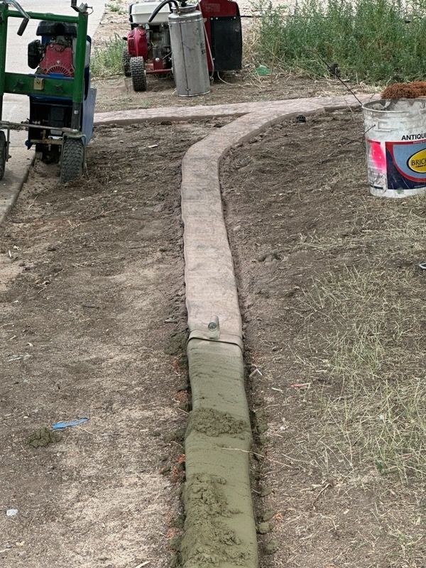 A narrow concrete path being constructed outdoors. A green machine and other equipment sit nearby.
