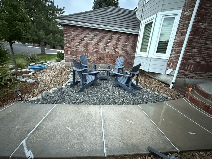 Concrete curb being installed outdoors in a dirt area; a bucket and tools are nearby.
