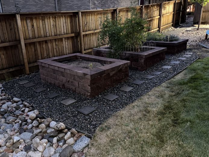 Lawn with a brick-like border separating green grass and a garden with plants, a solar light, and dark soil.