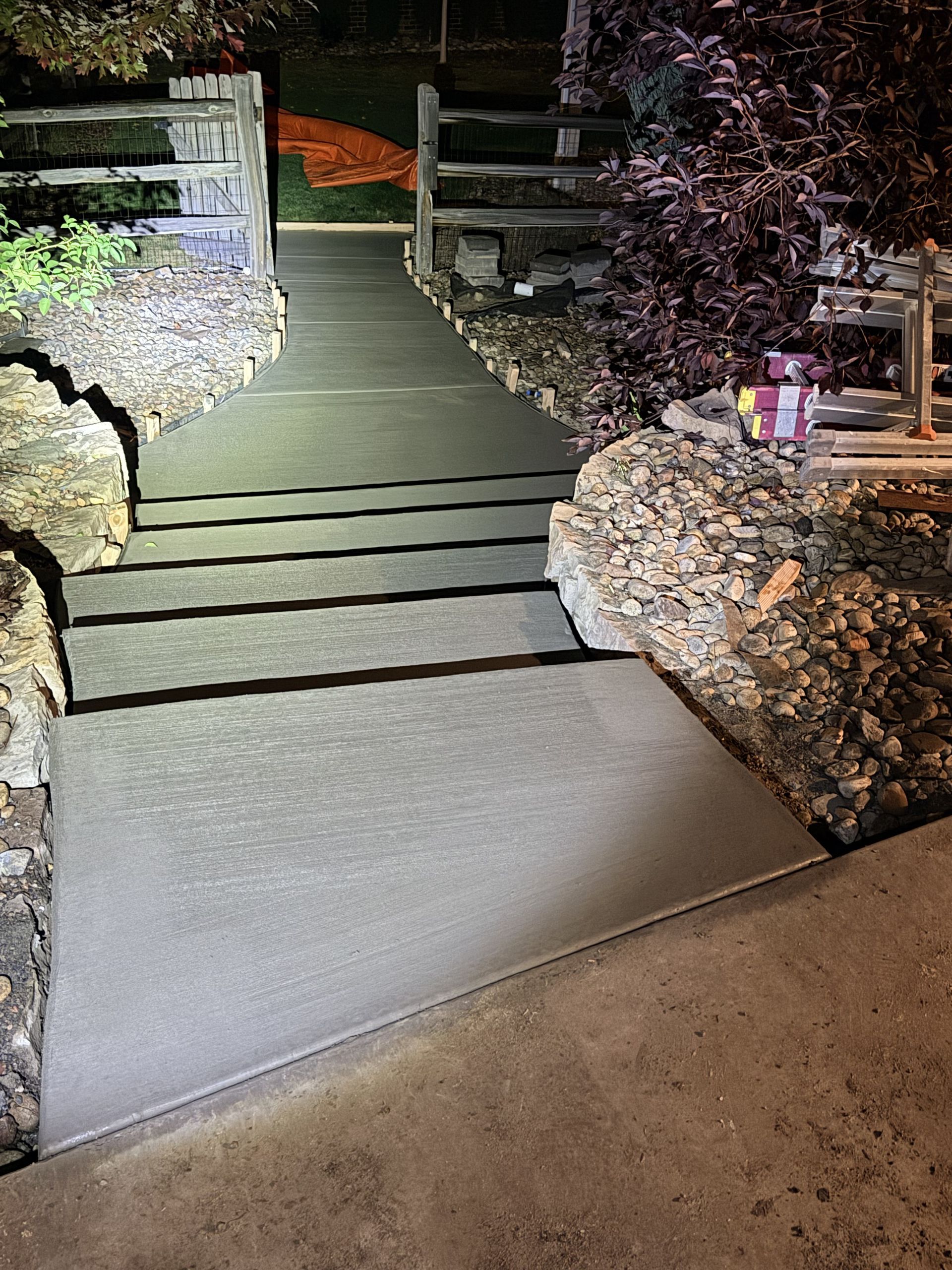 New concrete driveway section next to old sidewalk. A dark truck sits on the left, with trees and a house in the background.