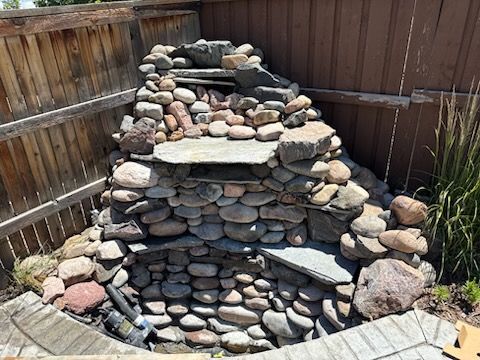 Rock waterfall structure built against a wooden fence in a yard.