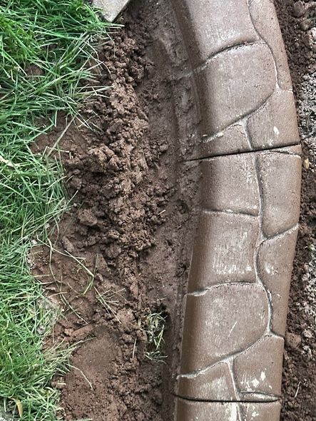 Brown concrete edging next to dirt and green grass.