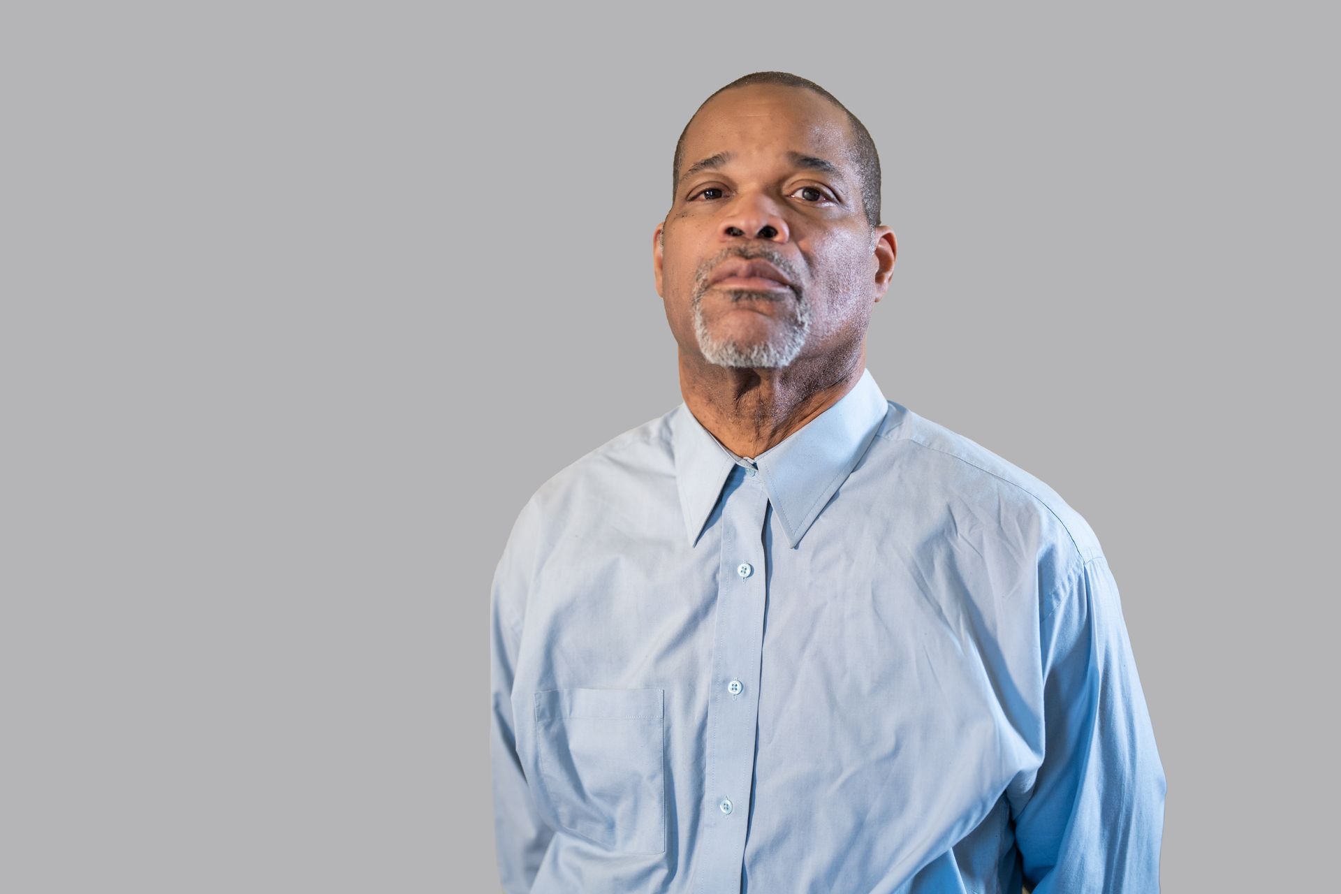 A man in a blue shirt is standing in front of a gray background.