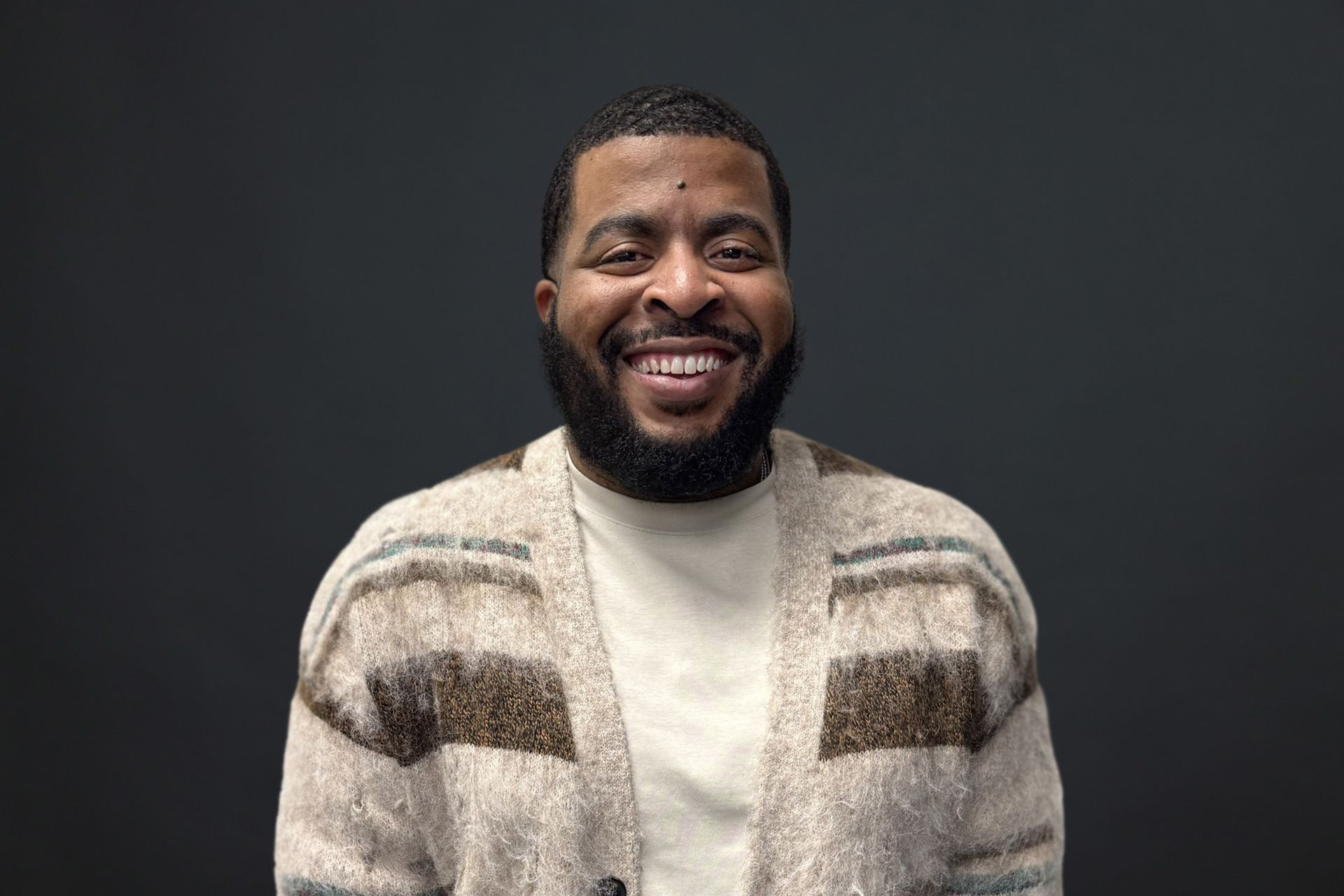 A man with a beard is wearing a sweater and smiling.