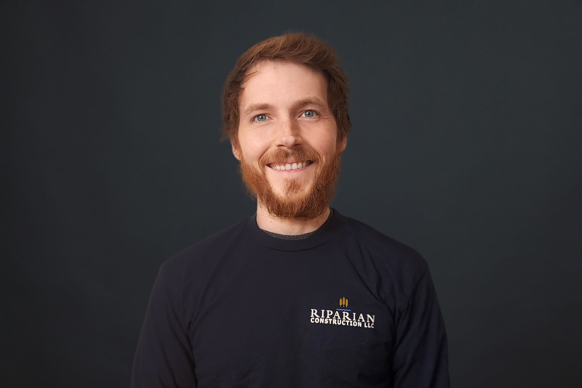 A man with a beard is wearing a black shirt and smiling.