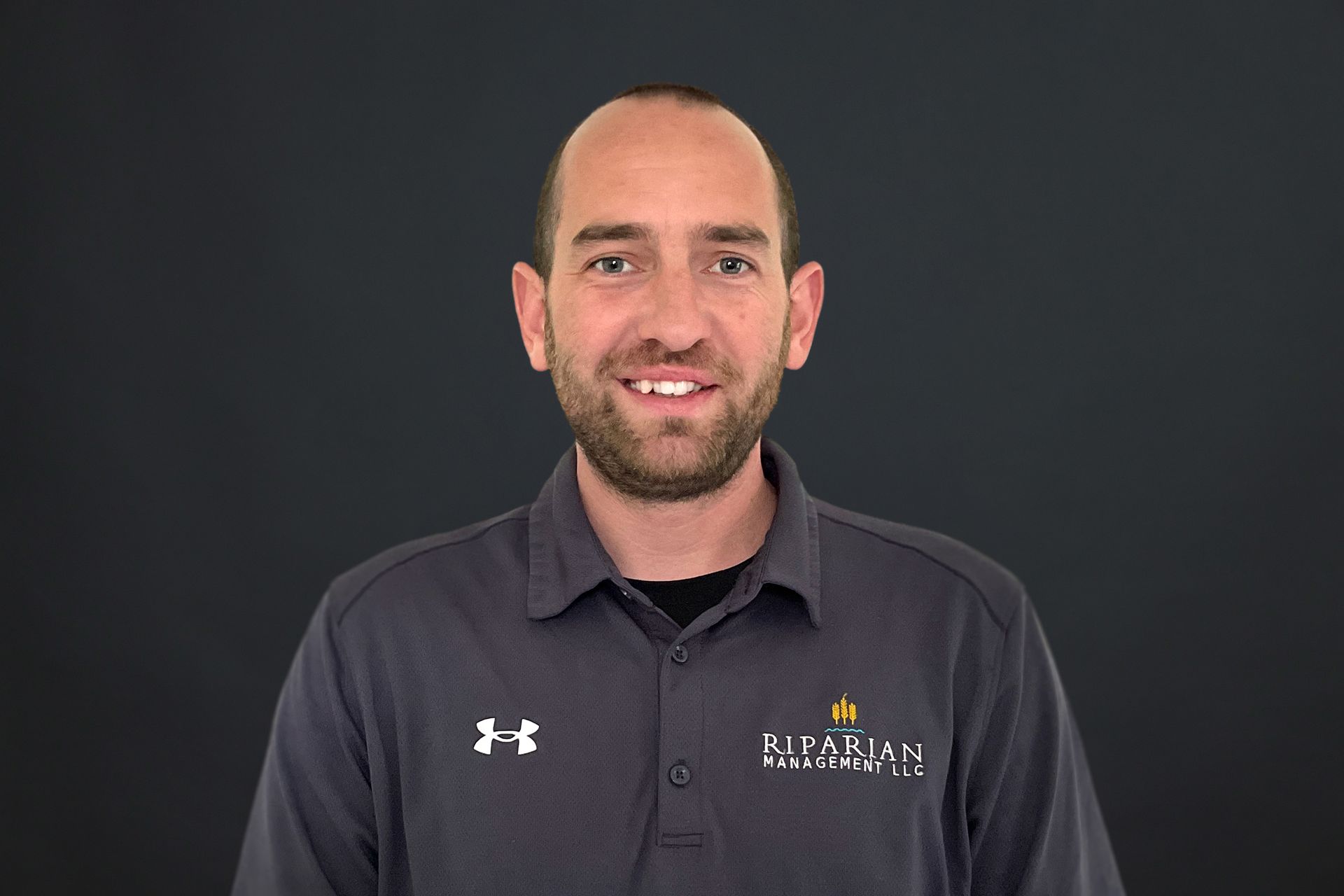 A man with a beard is wearing a gray under armour shirt.