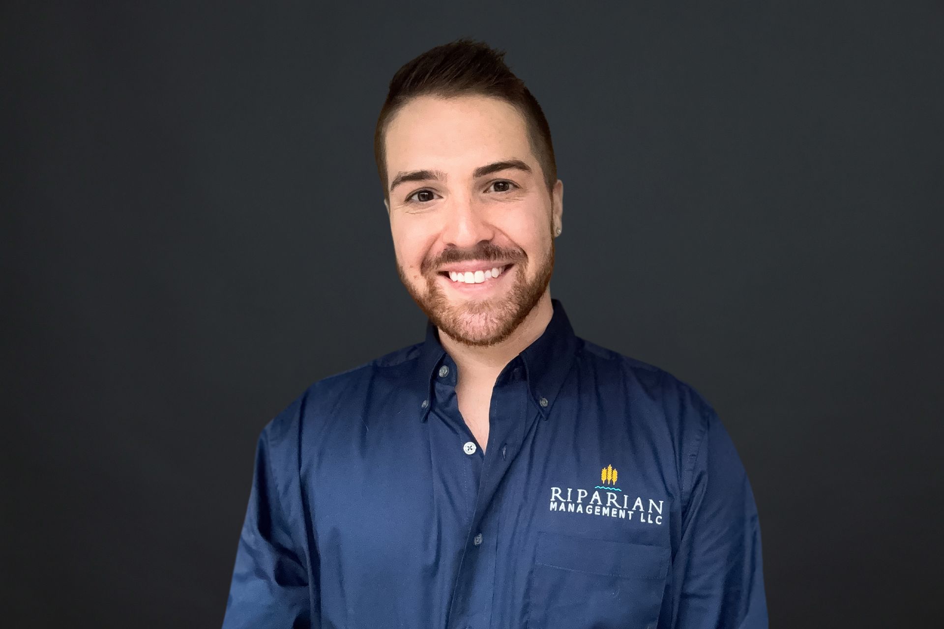 A man with a beard is wearing a blue shirt and smiling.