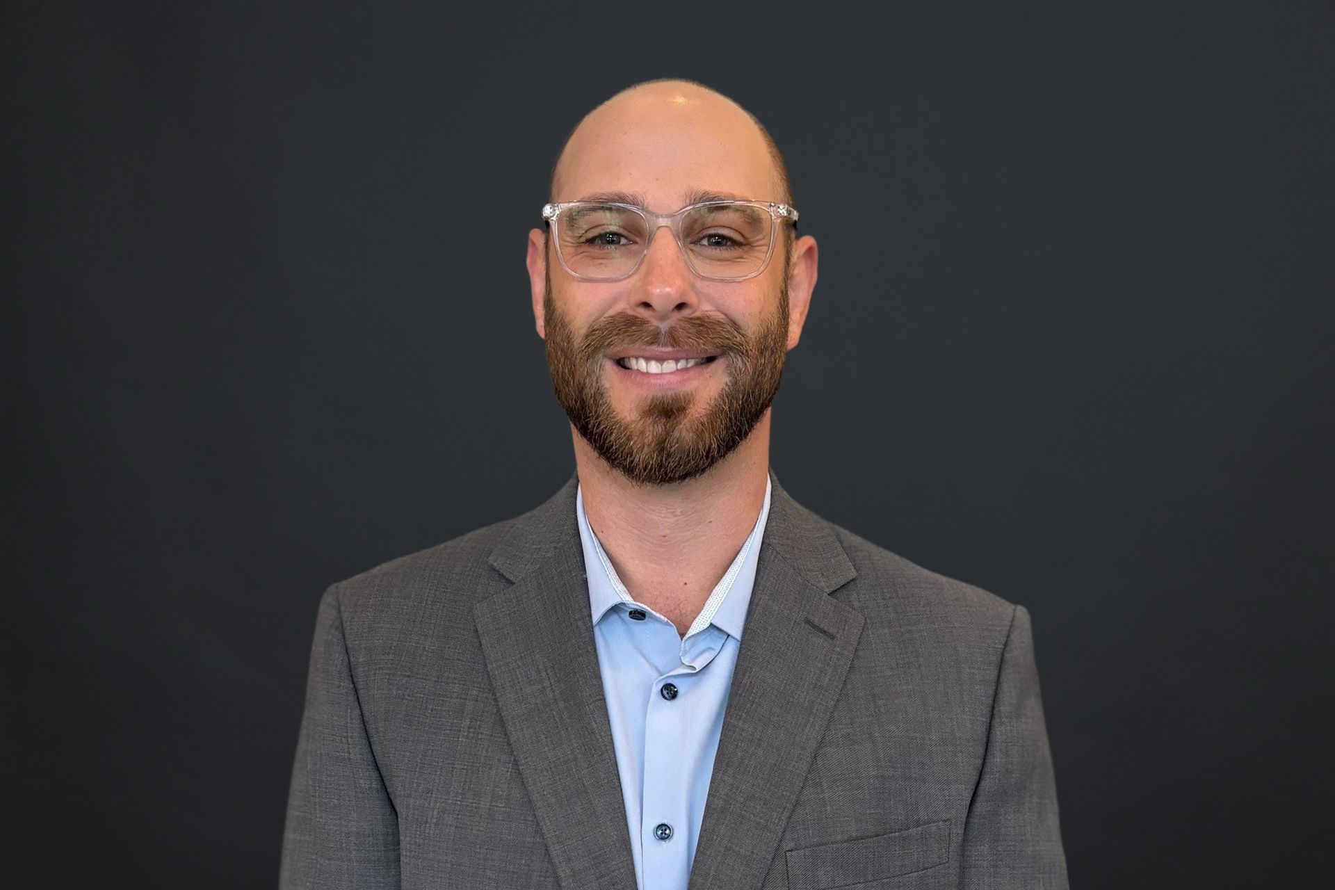 A bald man with a beard wearing glasses and a suit is smiling for the camera.