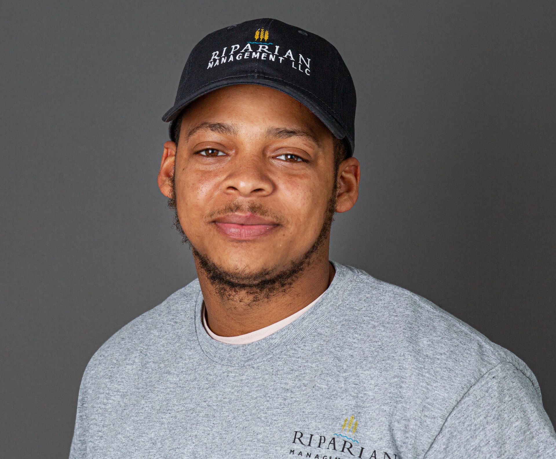 A man wearing a hat and a gray shirt is looking at the camera.