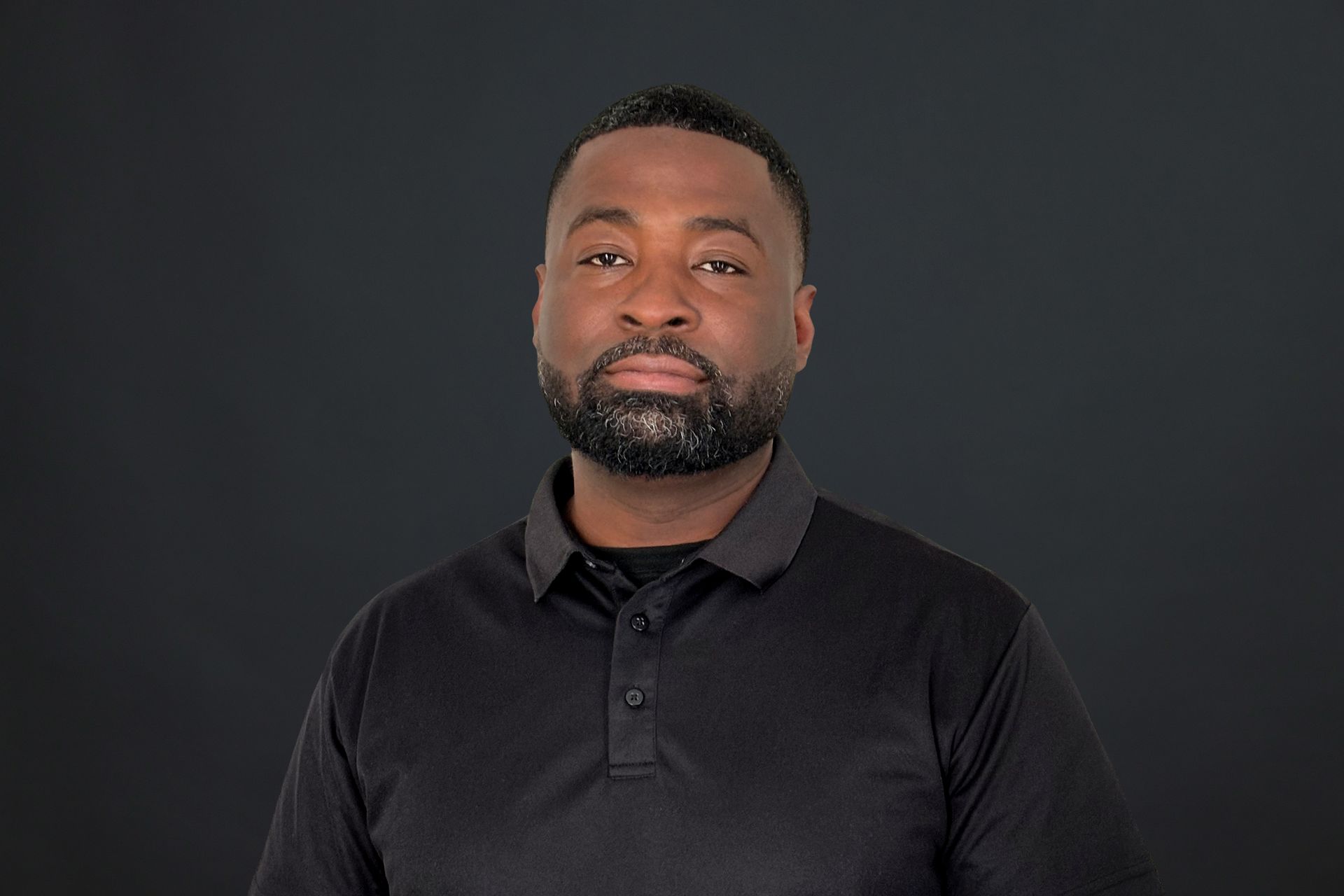A man with a beard is wearing a black shirt and looking at the camera.