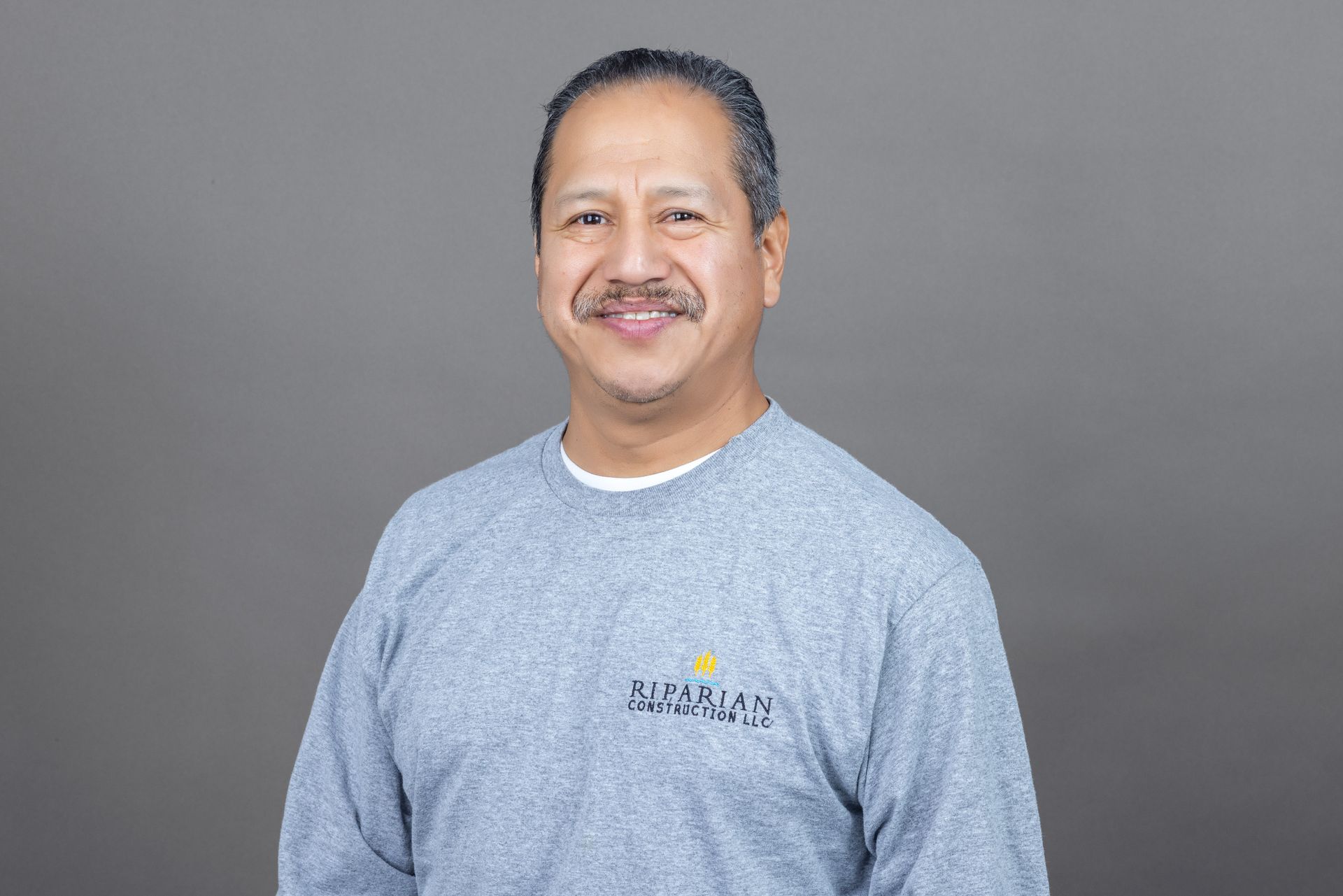 A man is wearing a grey sweater and smiling for the camera.