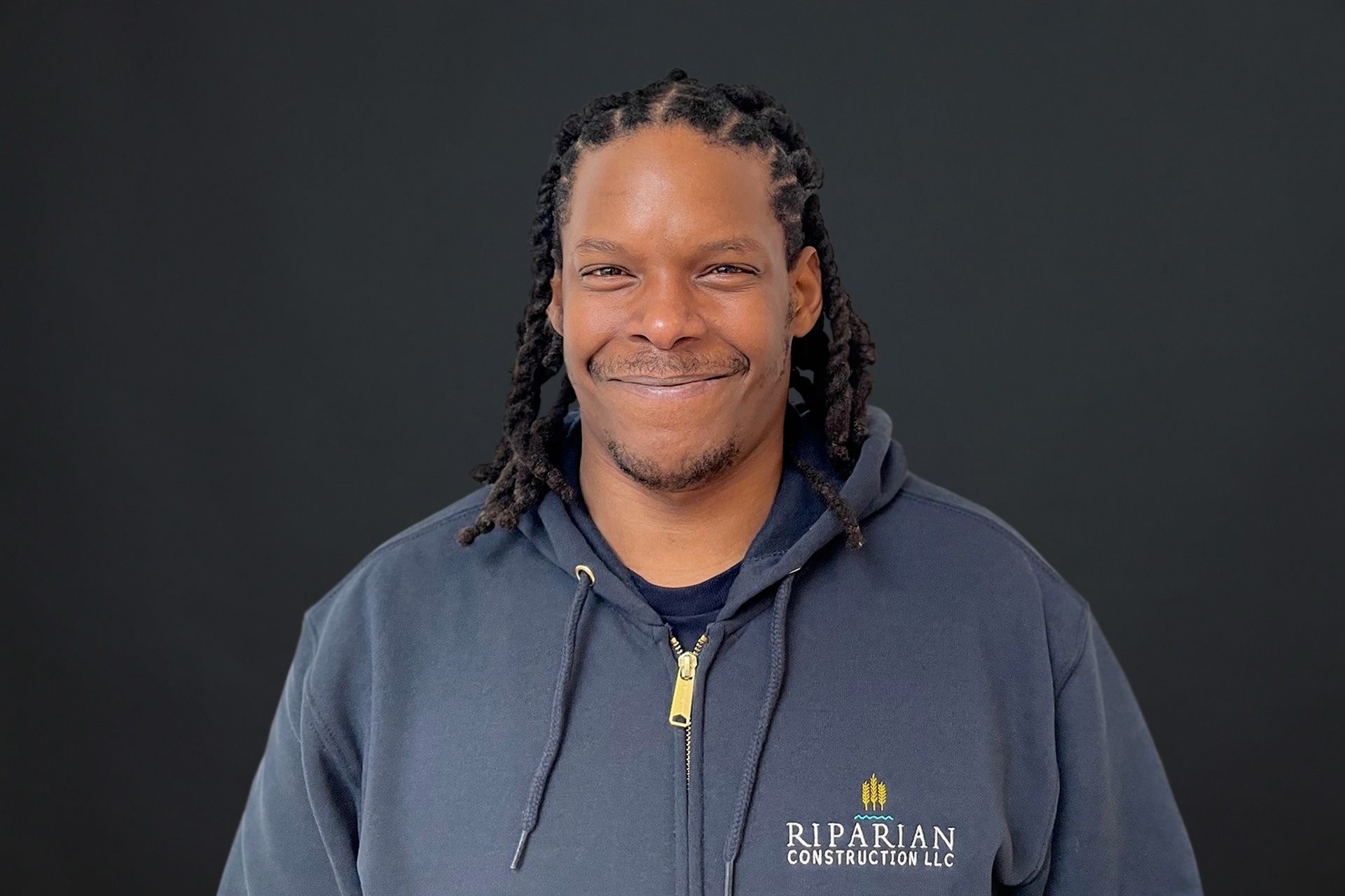 A man with dreadlocks is wearing a hoodie and smiling.