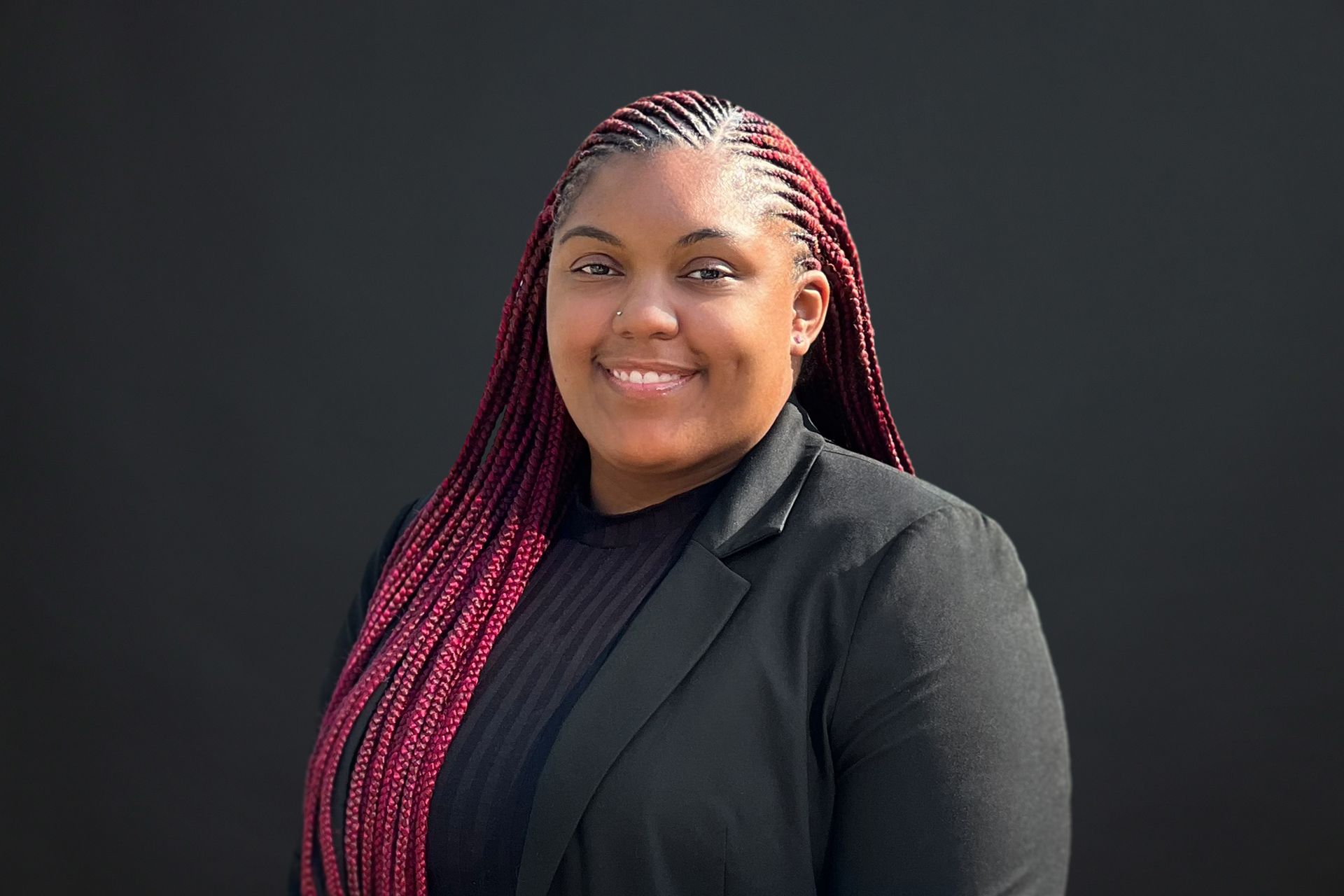 A woman with red braids is wearing a black jacket and smiling.