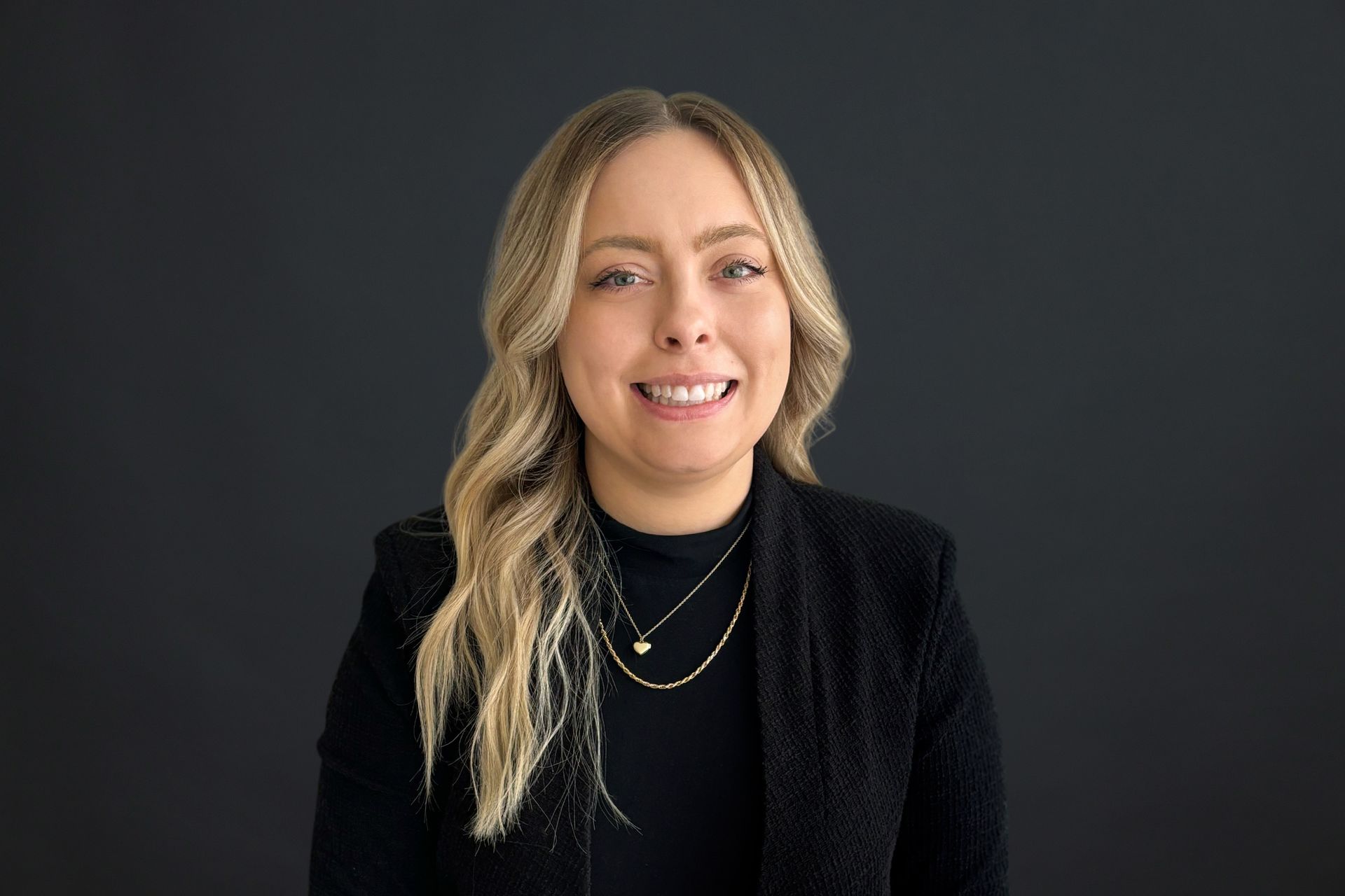 A woman in a black jacket and necklace is smiling for the camera.
