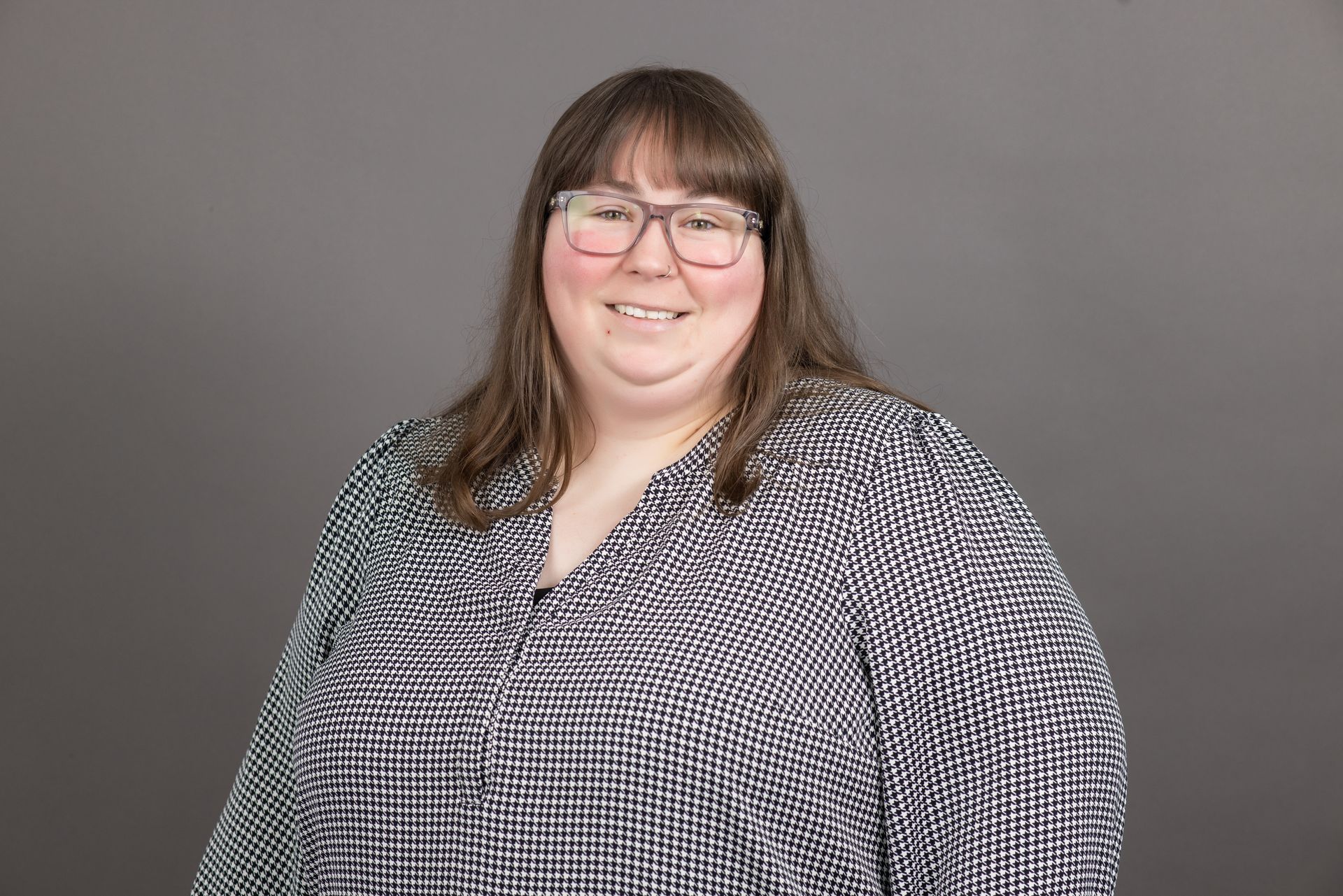 A woman wearing glasses and a black and white shirt is smiling for the camera.