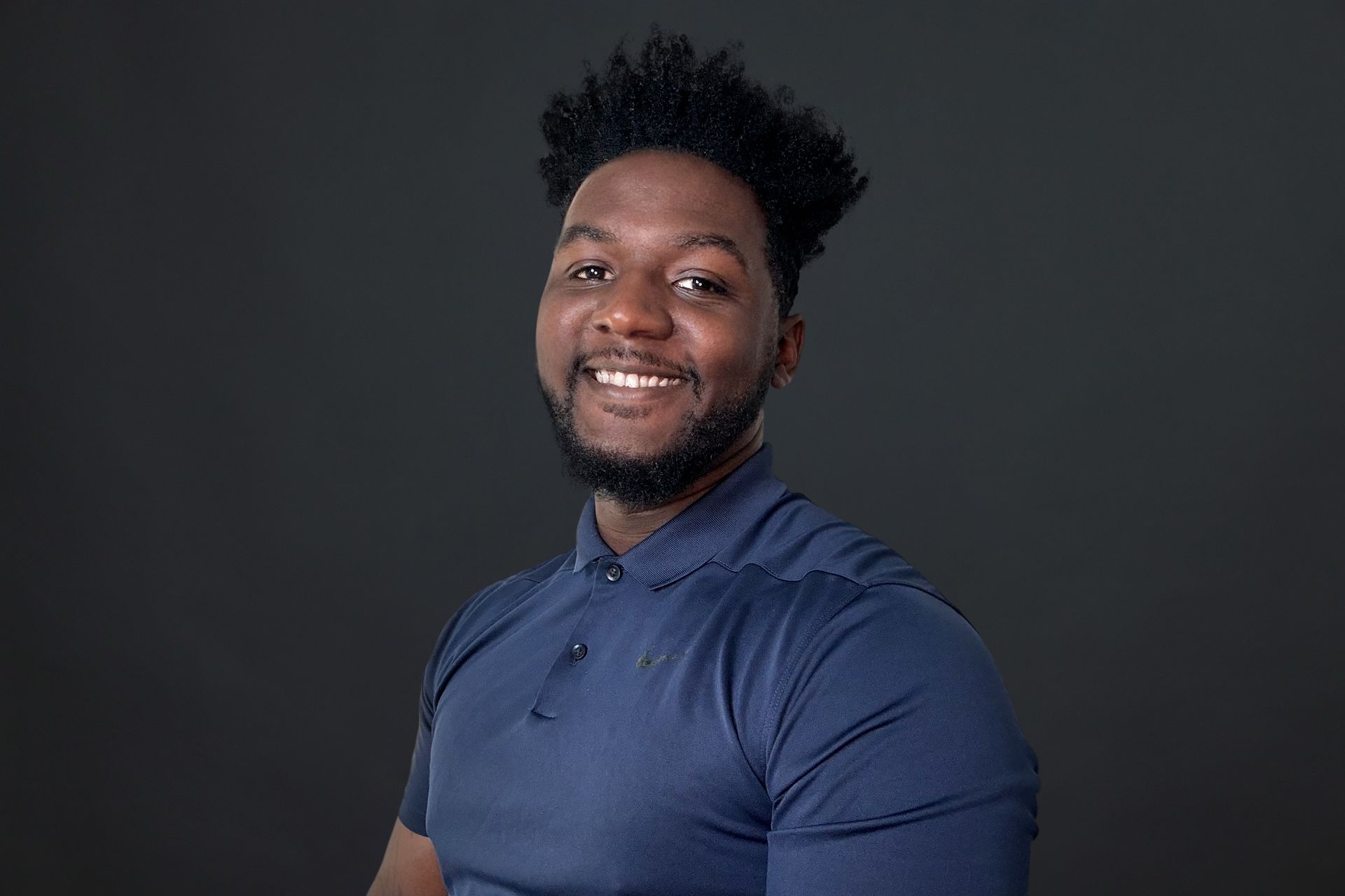 A man with a beard is wearing a blue shirt and smiling.