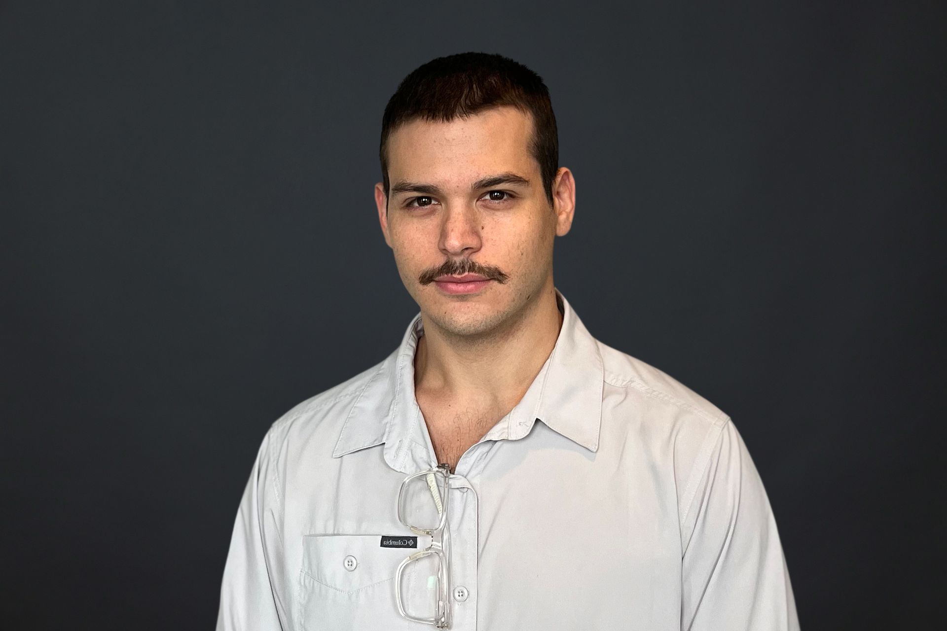 A man with a mustache and glasses is wearing a white shirt.