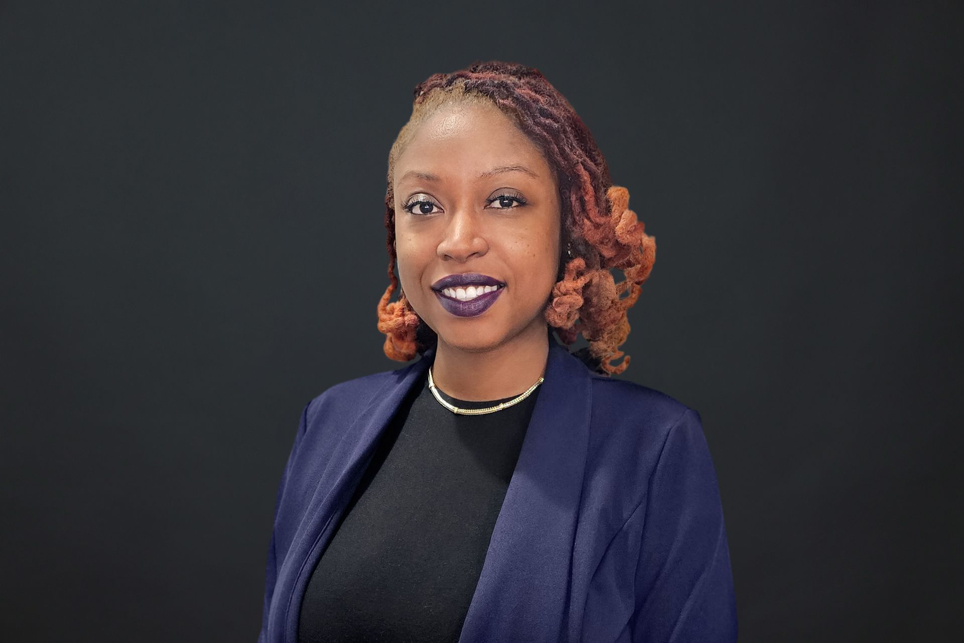 A woman wearing a purple jacket and a black shirt is smiling for the camera.