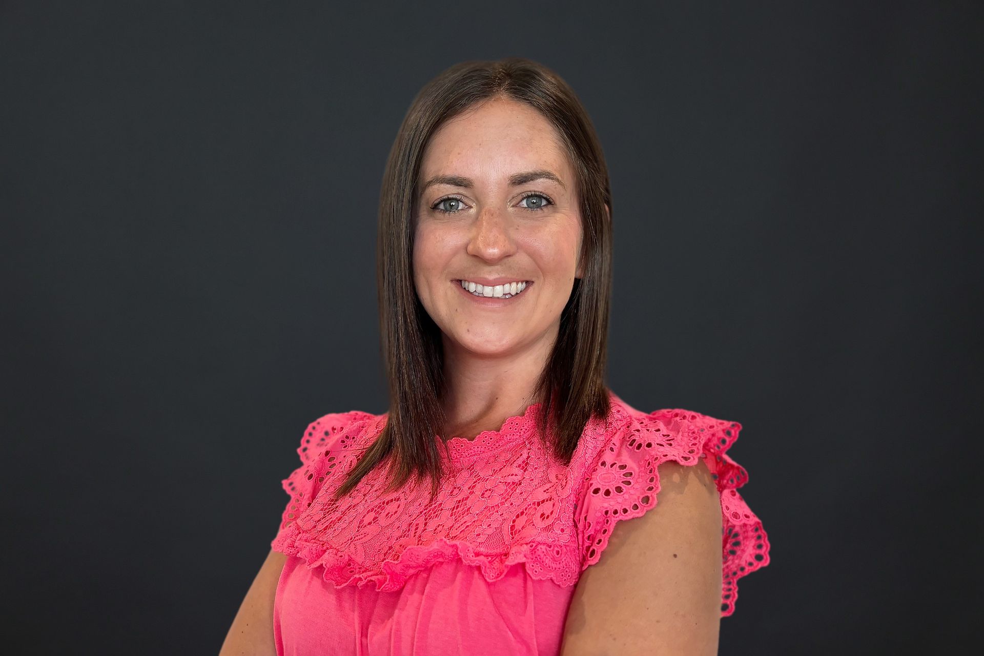 A woman in a pink dress is smiling and standing with her arms crossed.