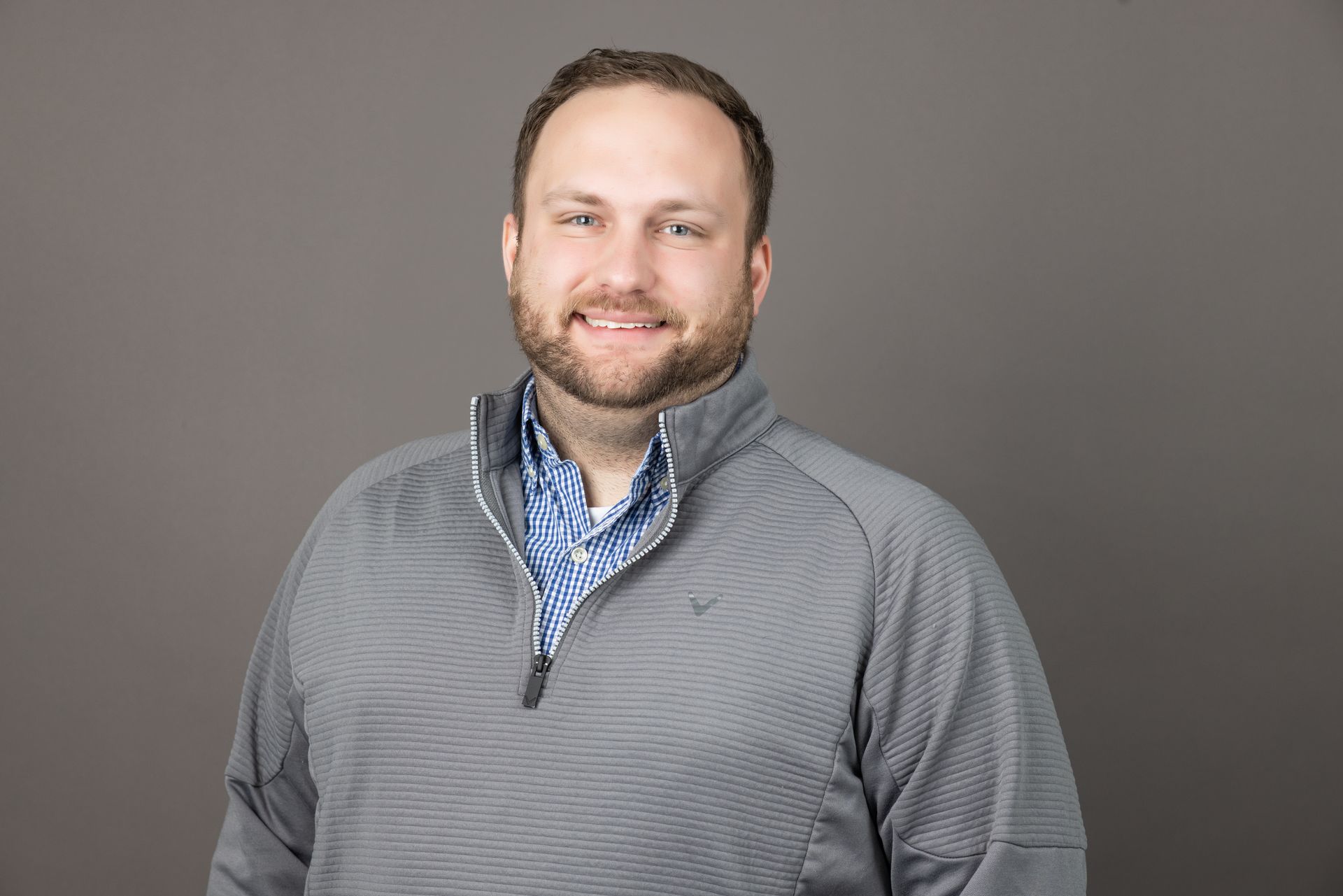 A man with a beard is wearing a gray sweater and a blue shirt.