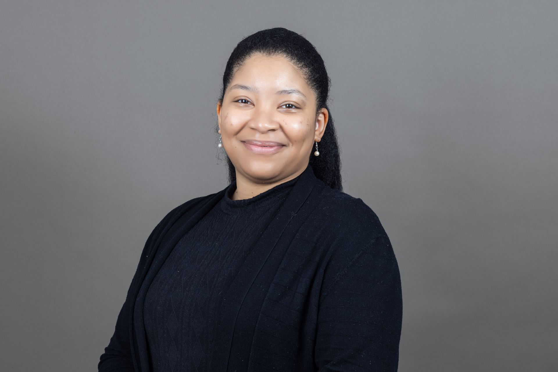 A woman wearing a black sweater and earrings is smiling for the camera.