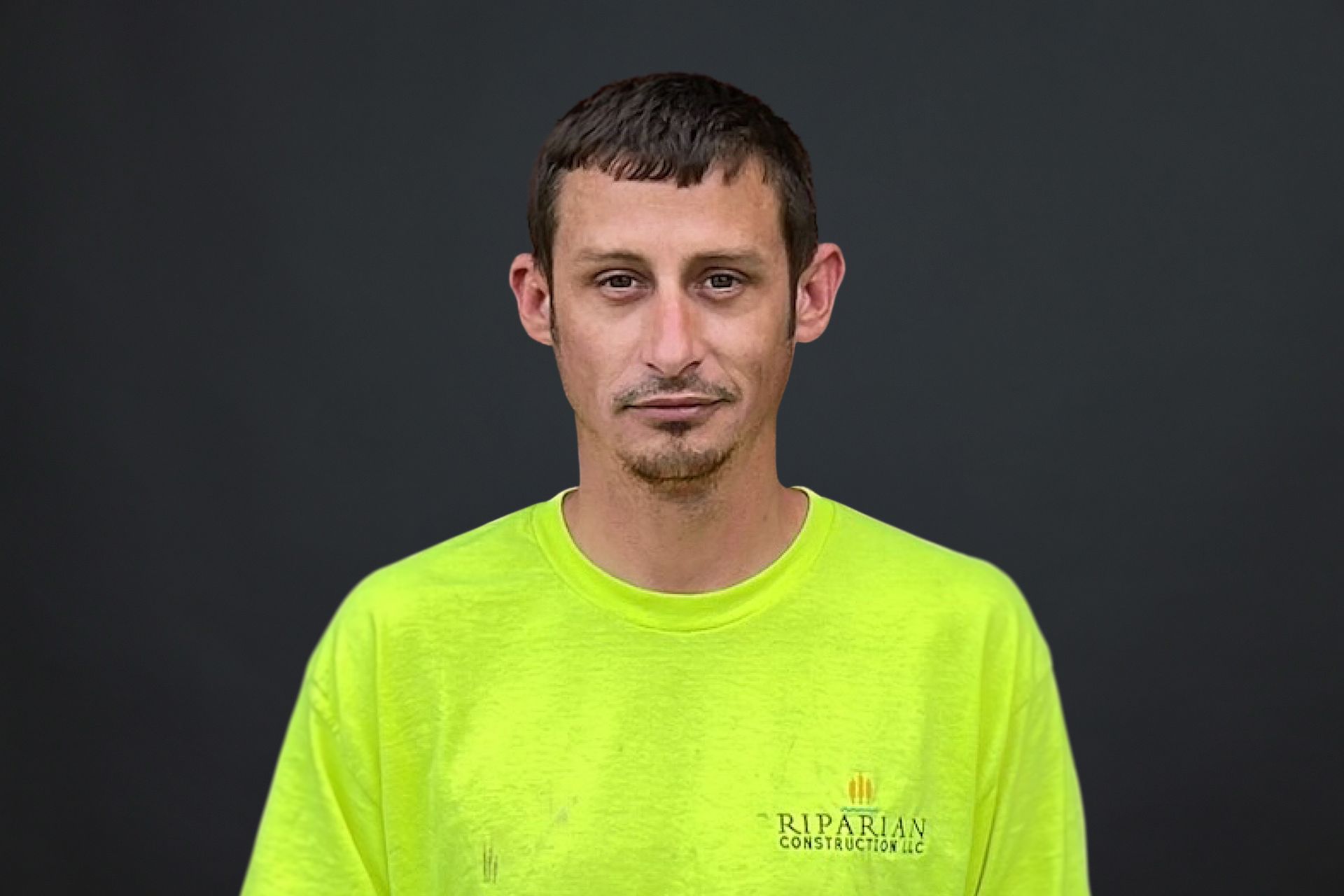 A man wearing a neon yellow t-shirt is standing in front of a black background.