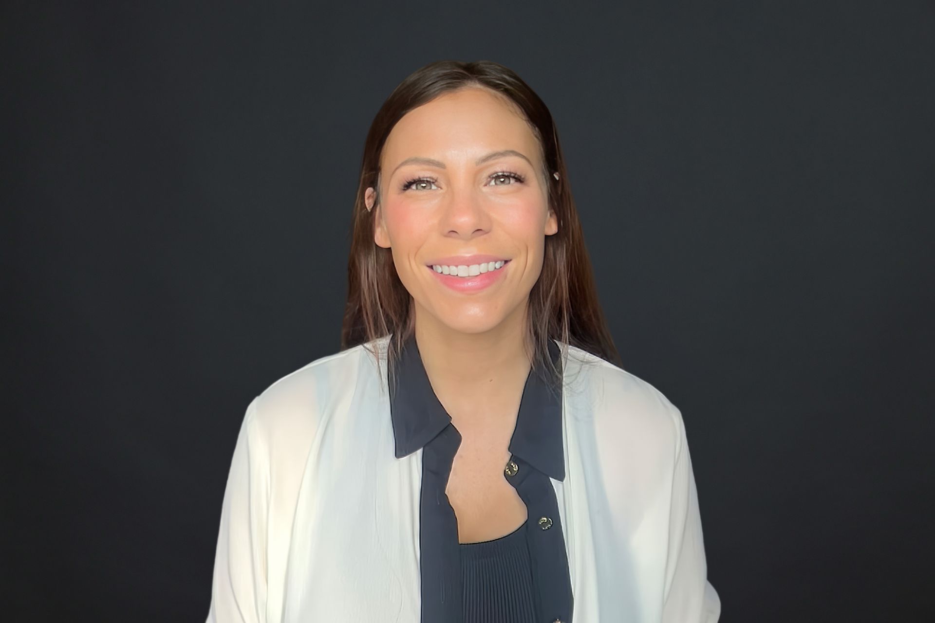 A woman wearing a white shirt and a black shirt is smiling.