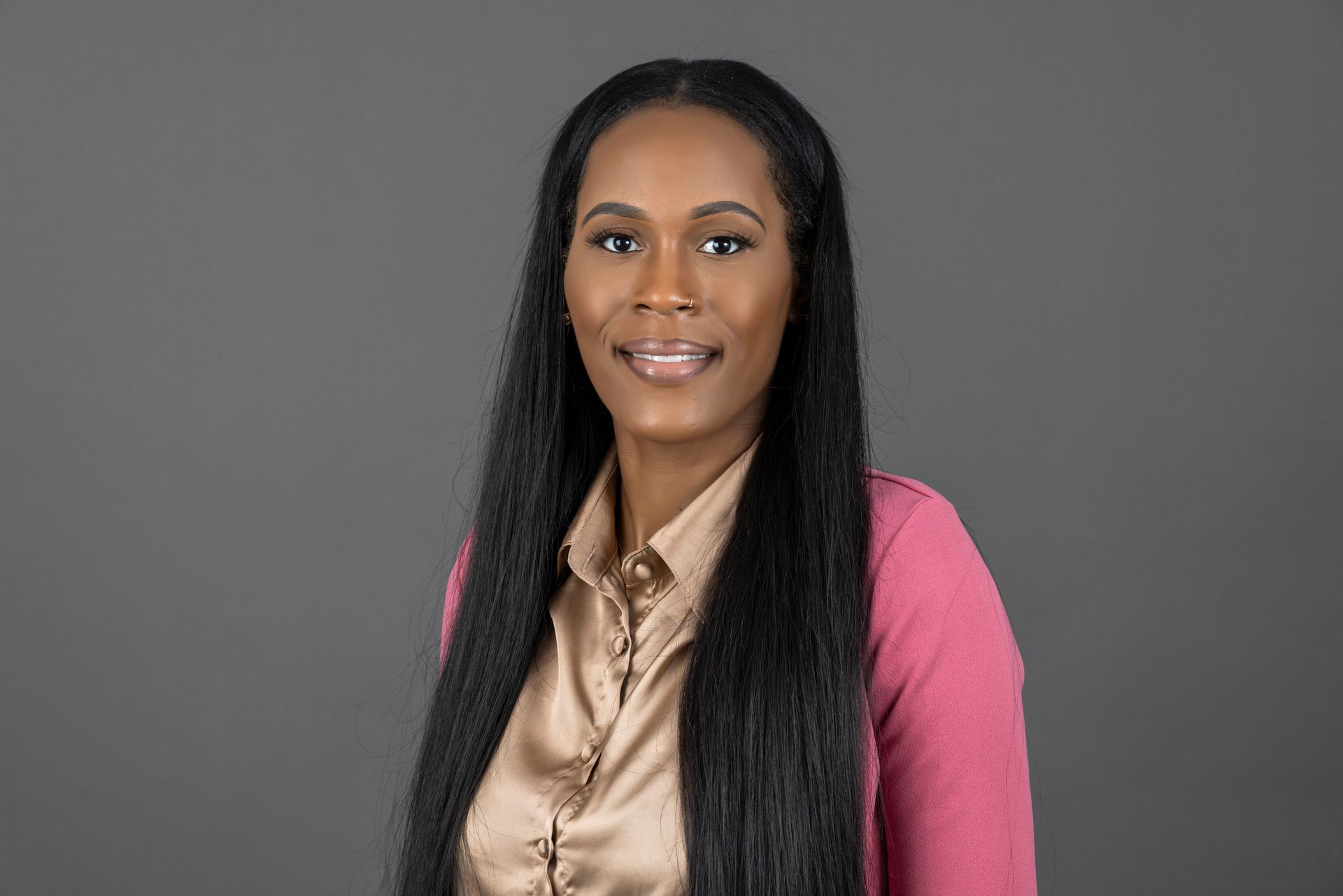 A woman with long black hair is wearing a pink sweater and a tan shirt.